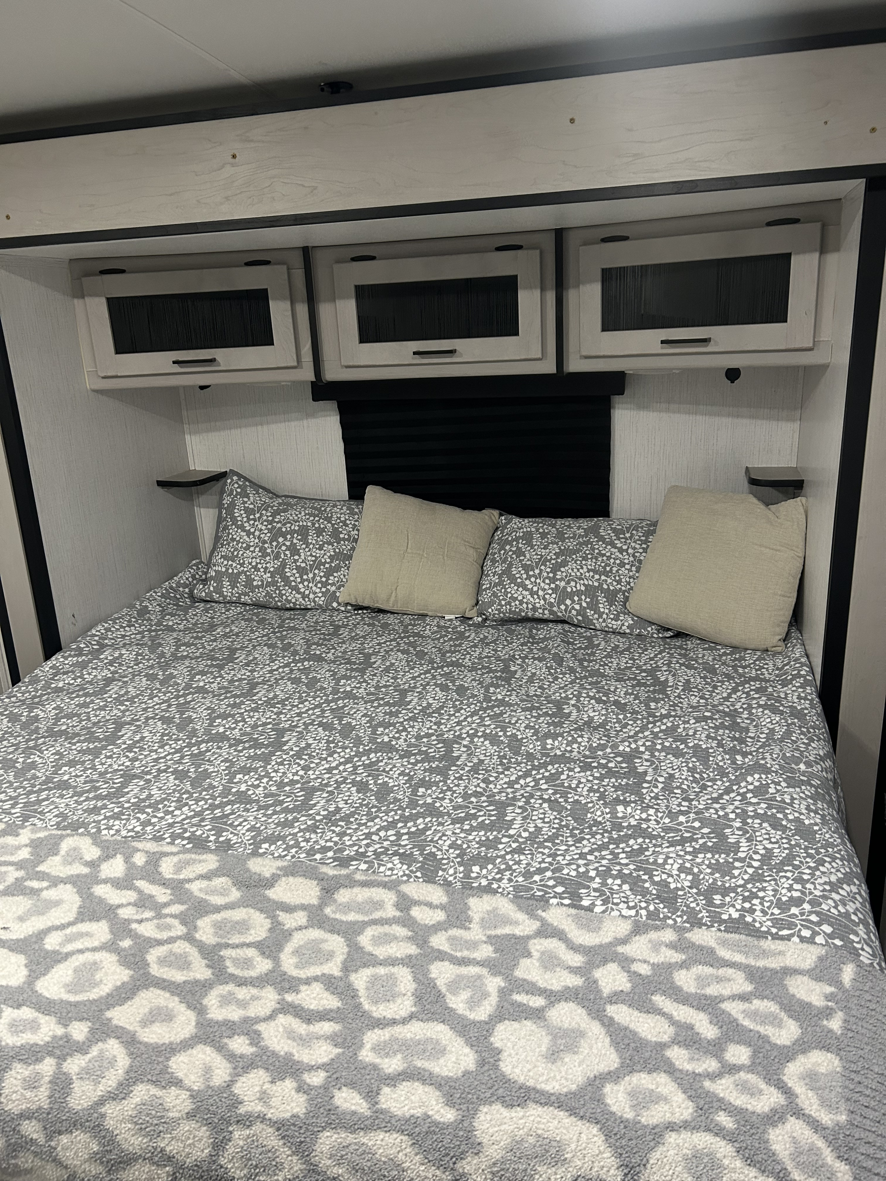 Cozy RV rental bedroom with gray patterned bed, beige pillows, and modern overhead cabinets for a compact, stylish space.. Heartland RVs Mallard 2023