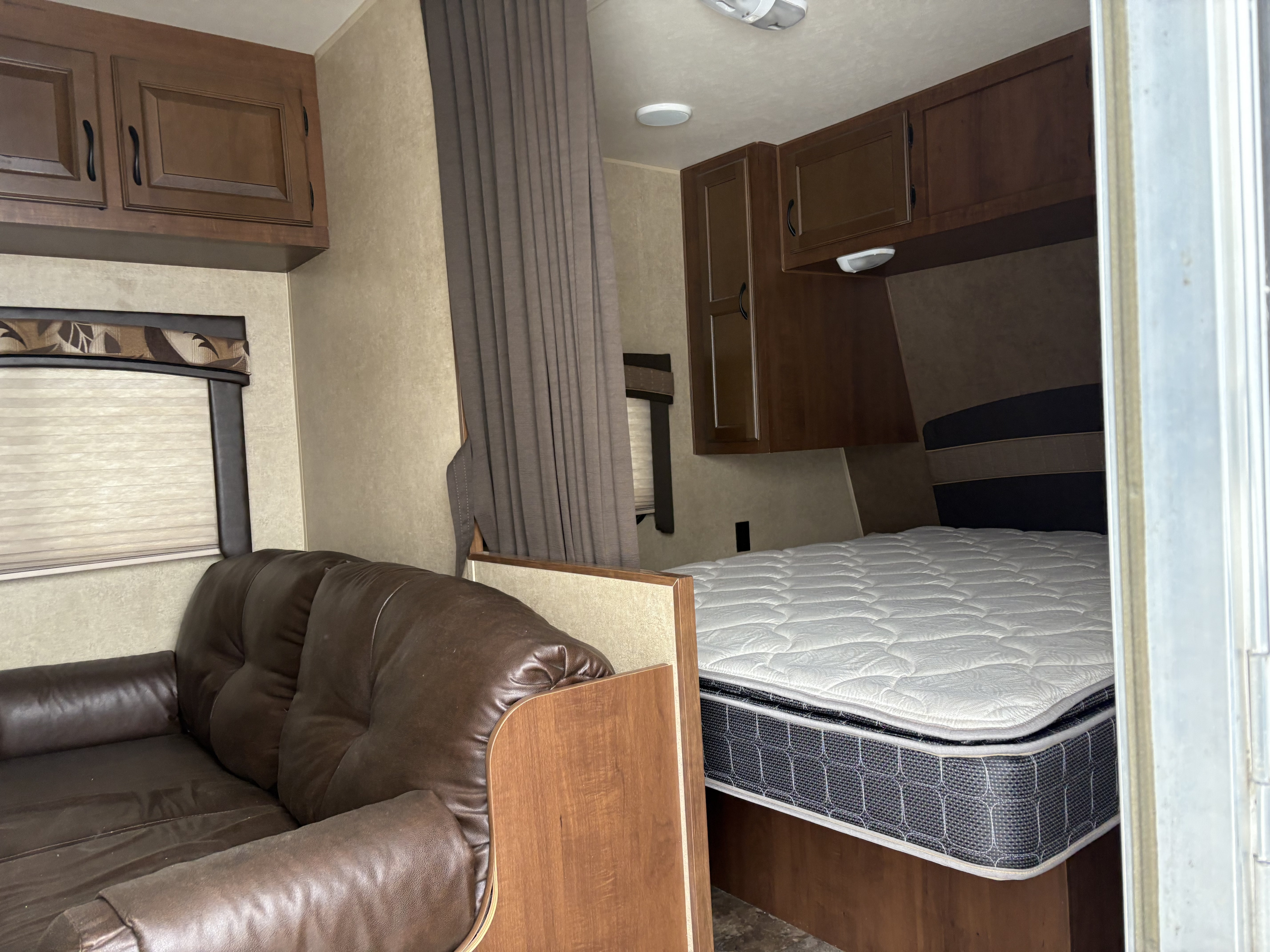 RV rental interior showing a cozy bed, brown leather sofa, wood cabinets, and window with blind.. Jayco Jay Flight 2014
