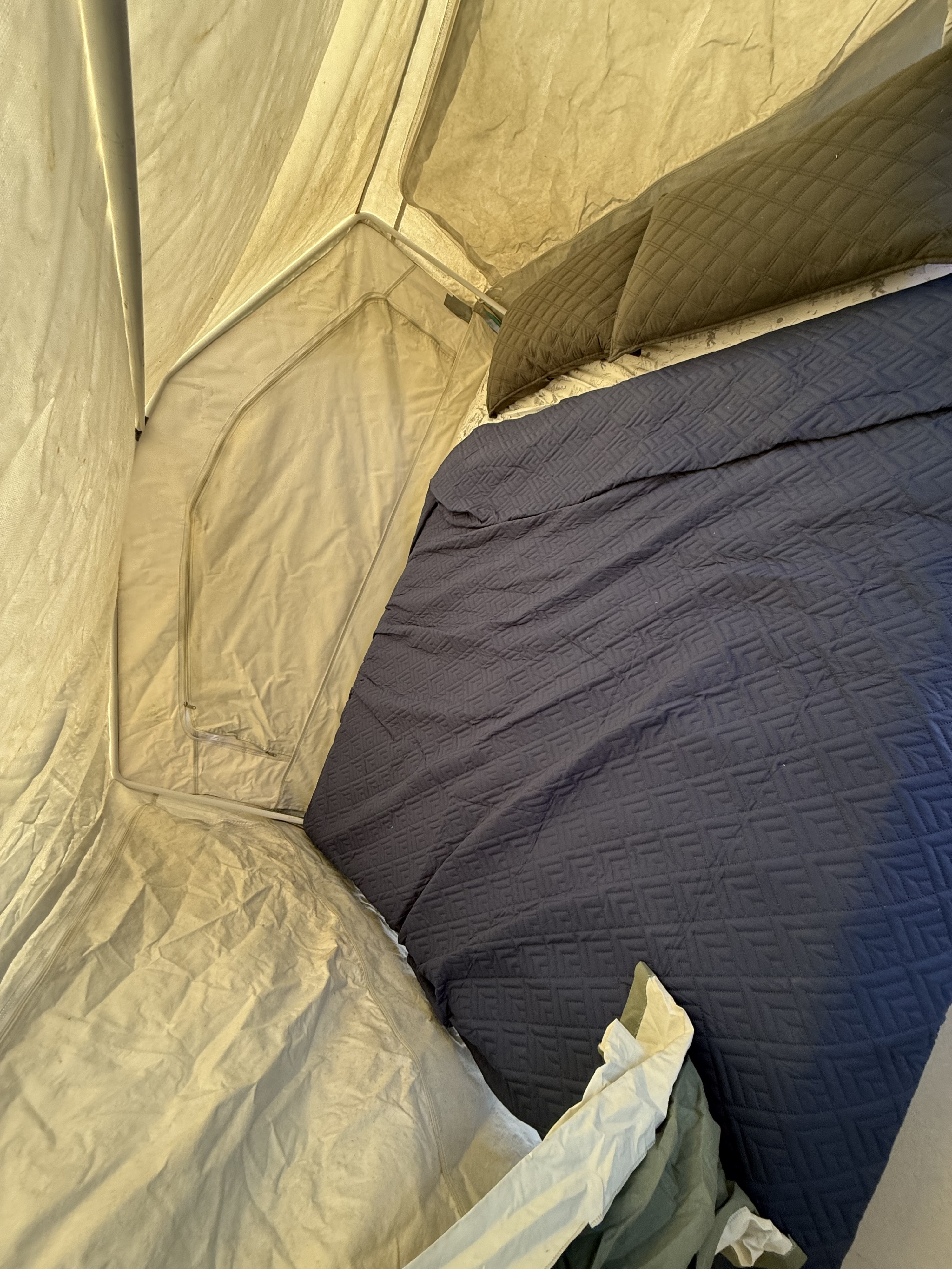 Inside a comfortable rv rental, featuring a bed with navy blue quilted bedding and light beige fabric walls. Ready for travel!. Forest River Rockwood Freedom 2003