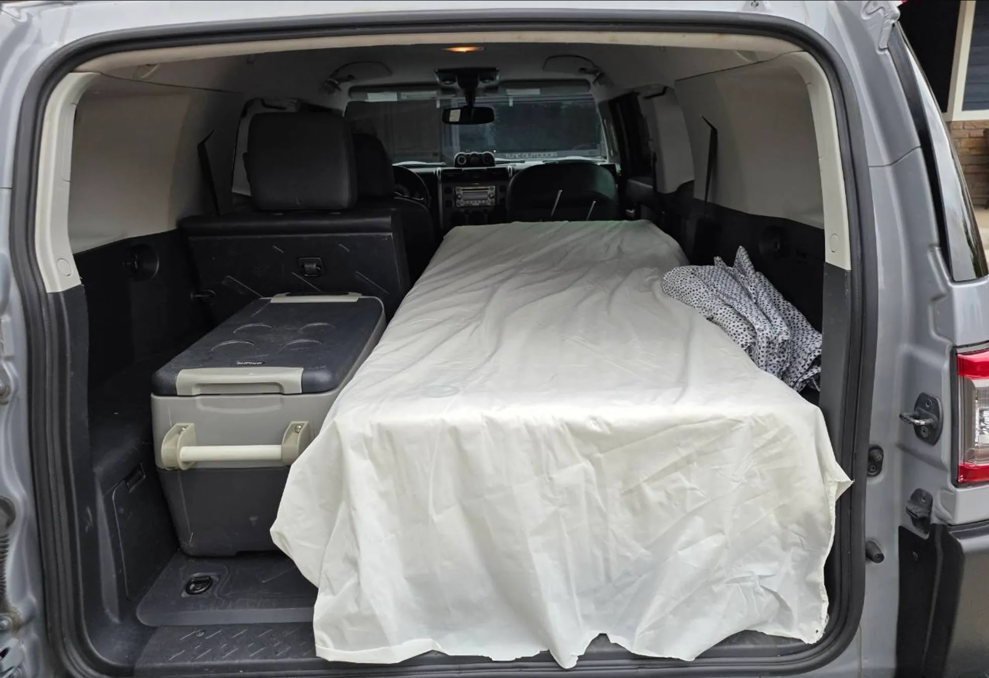Inside a grey SUV, a comfortable mattress and cooler create a practical car camping setup, ideal for an rv rental alternative.. Toyota FJ Cruisers Trail Teams 2013