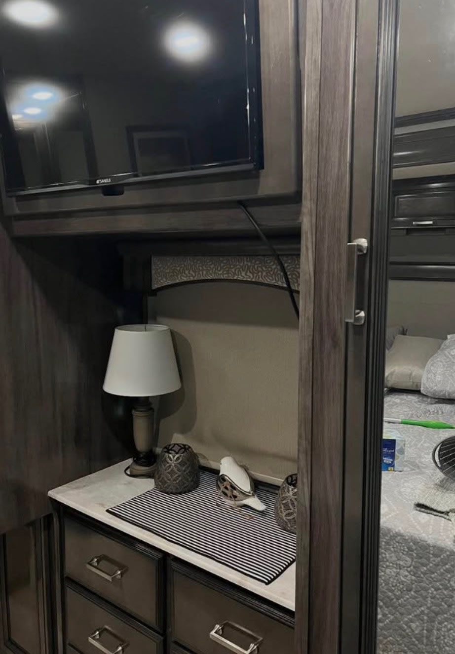 Cozy RV rental bedroom interior with a mounted TV, dresser, lamp, and a bed visible through a mirrored doorway.. Fleetwood Southwind 2020