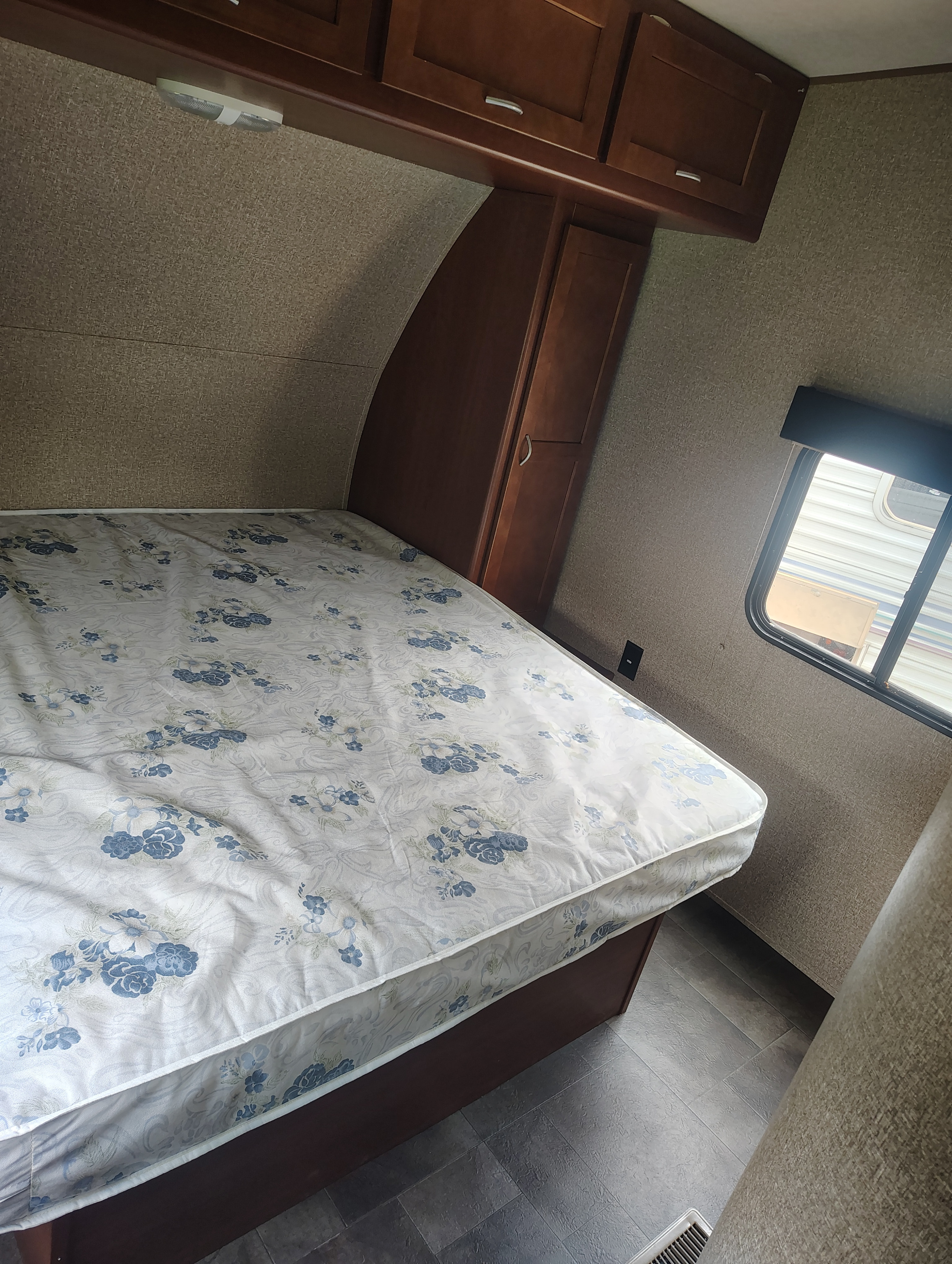 Cozy RV rental bedroom with a floral mattress, overhead wood cabinets, and a window, offering comfortable travel accommodations.. Forest River Vengeance 2015