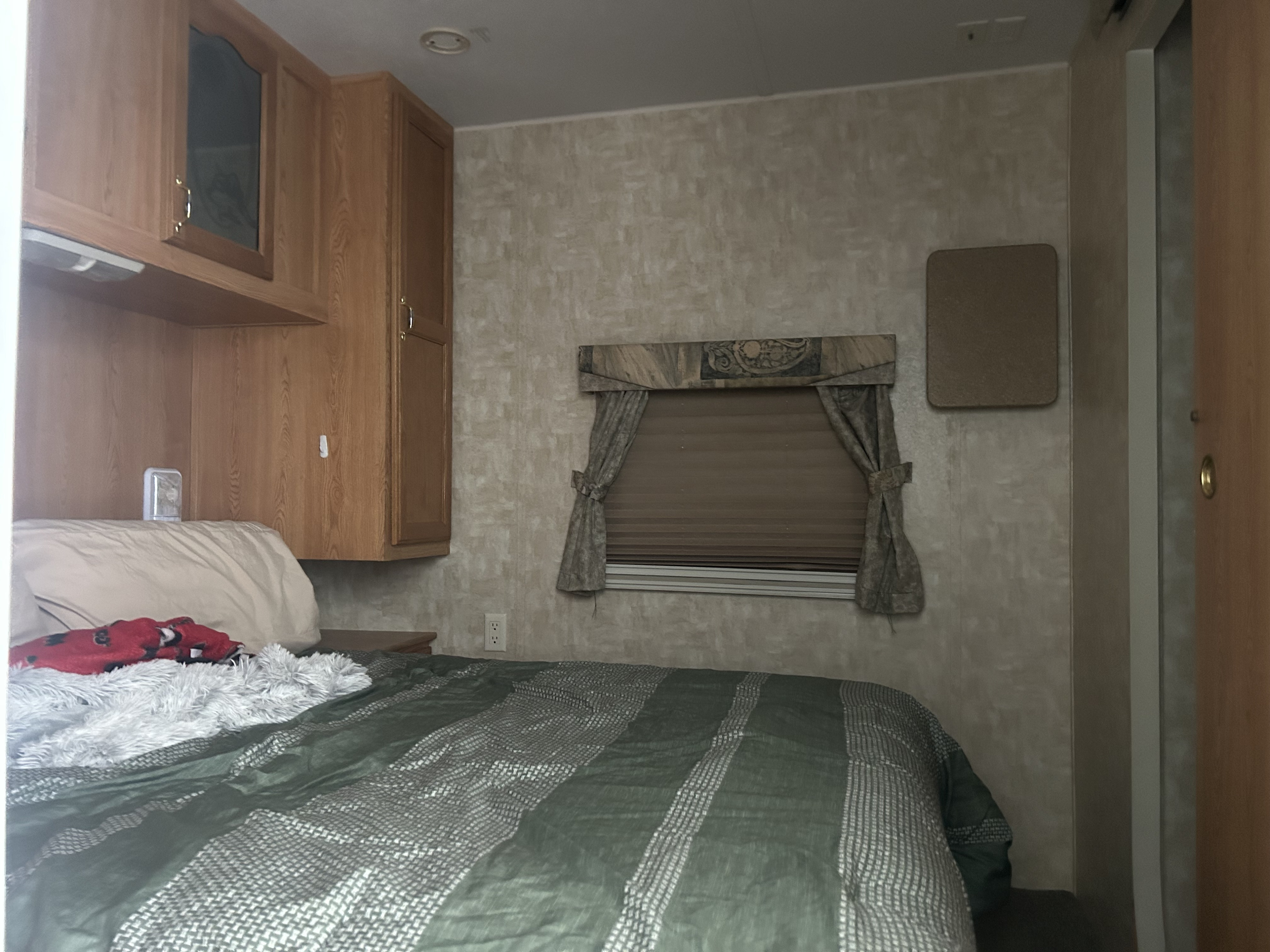 Inside an rv rental: a cozy bedroom with wooden cabinets, patterned wallpaper, striped bedding, and a window with blinds.. Forest River Cherokee 2007