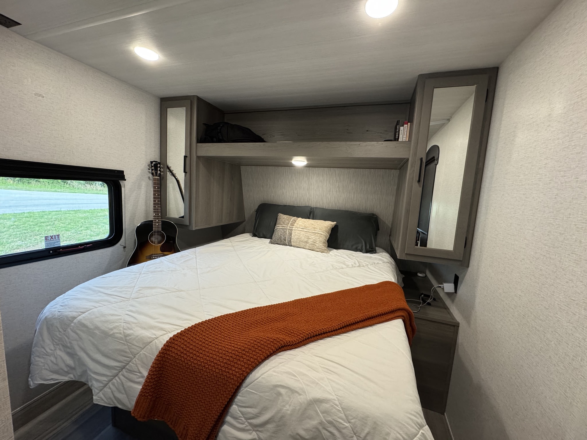 Cozy RV rental bedroom featuring a comfortable bed with a warm throw, guitar, and built-in overhead storage.. Keystone RV Hideout Sport 2024