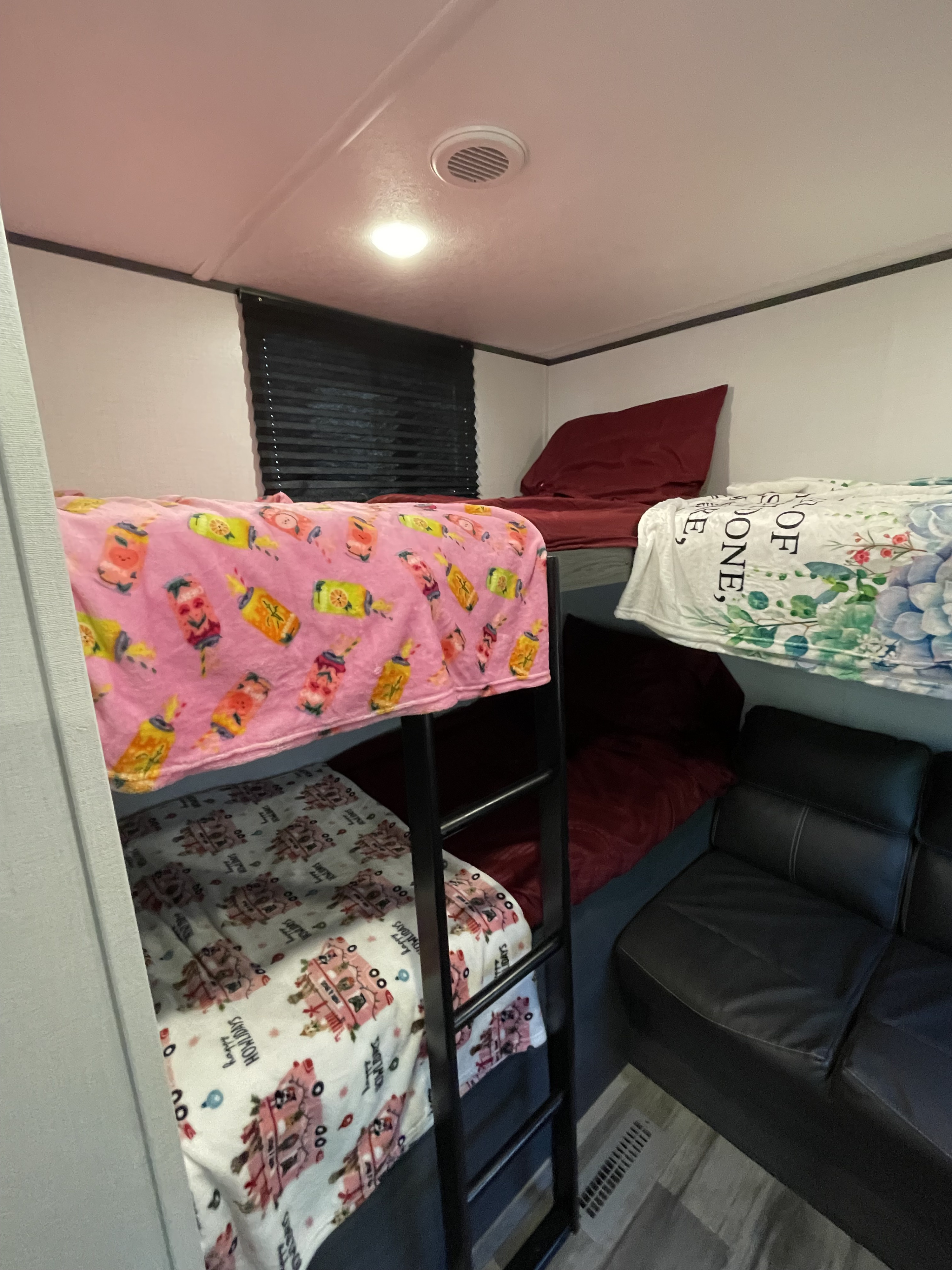 RV rental interior: A compact sleeping area features multiple bunk beds with colorful blankets and a black leather couch.. Dutchmen Colorado 29BHC 2025