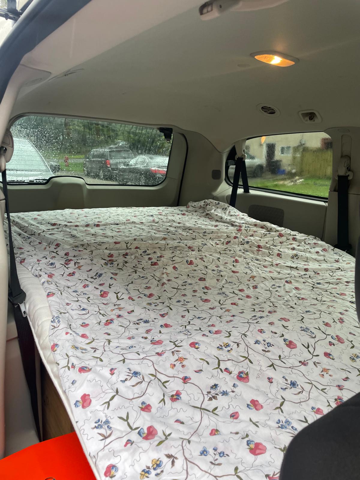 Inside an RV rental: a cozy car camping bed with a floral mattress, filling the vehicle's rear for road trips.. Dodge Grand Caravan 2011