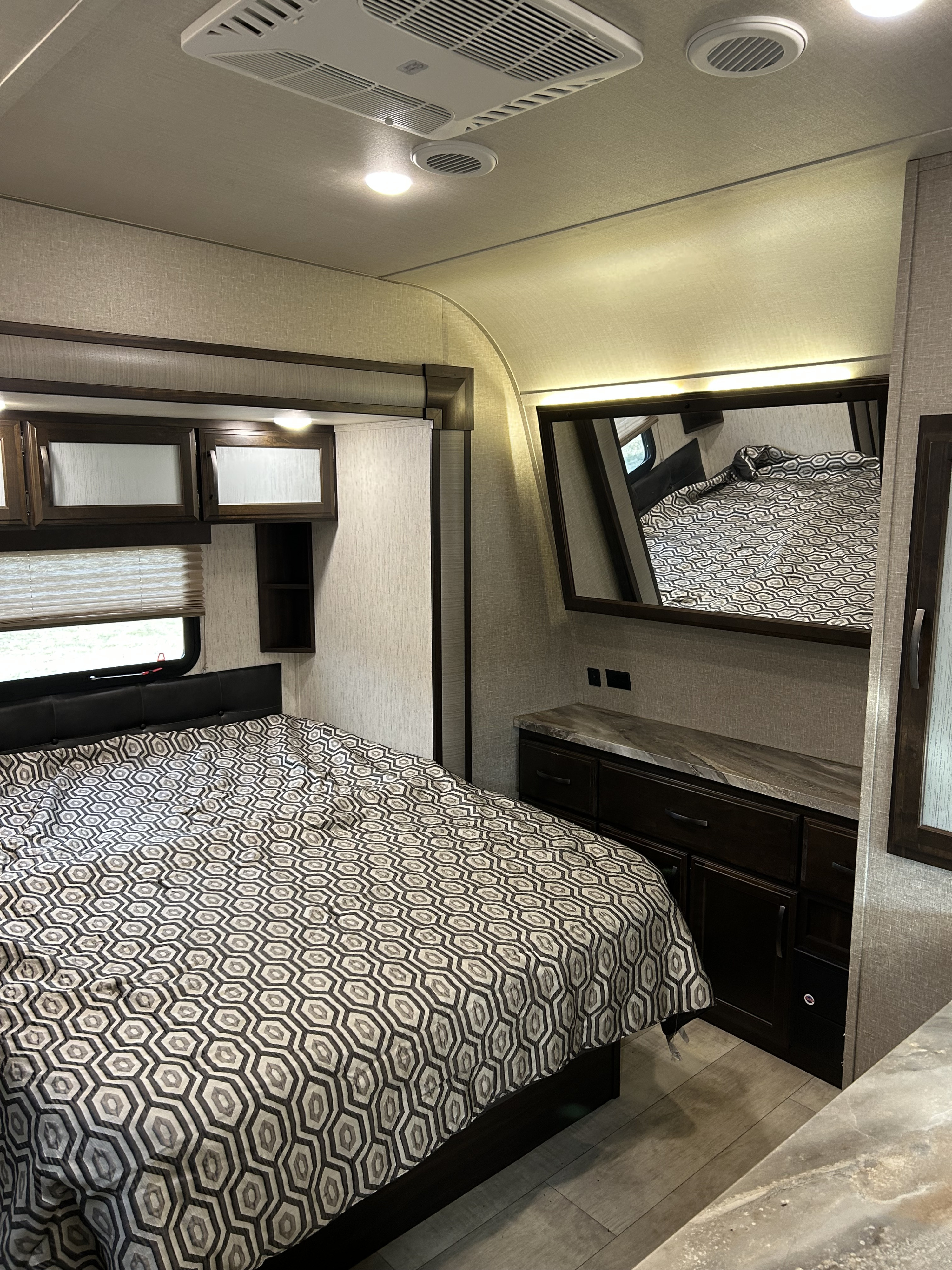 Inside an RV rental: a modern bedroom with a hexagon-patterned bed, built-in storage, mirror/TV, and sleek finishes.. Grand Design Momentum 2020