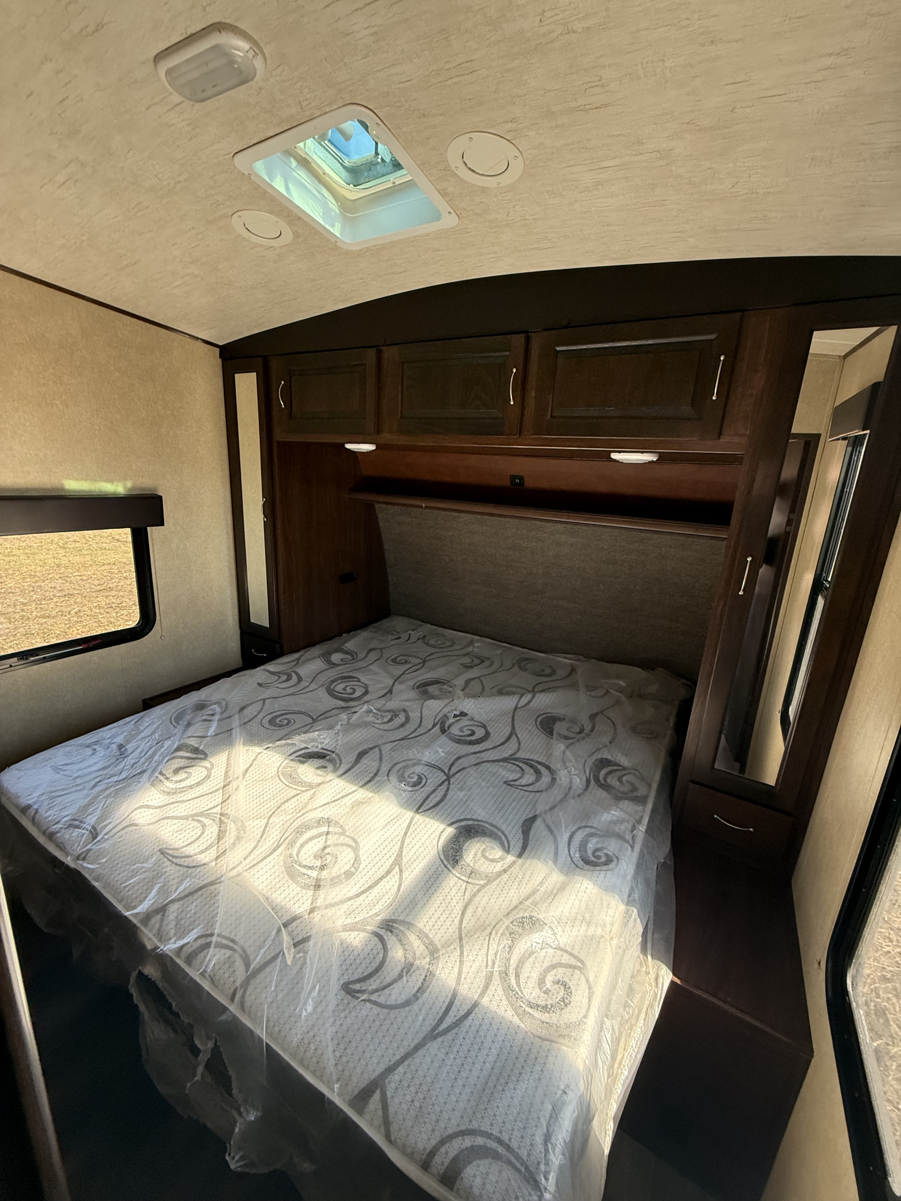 RV rental bedroom with a plastic-covered bed, overhead cabinets, ceiling vent, and a window letting in sunlight.. Heartland Torque 2016