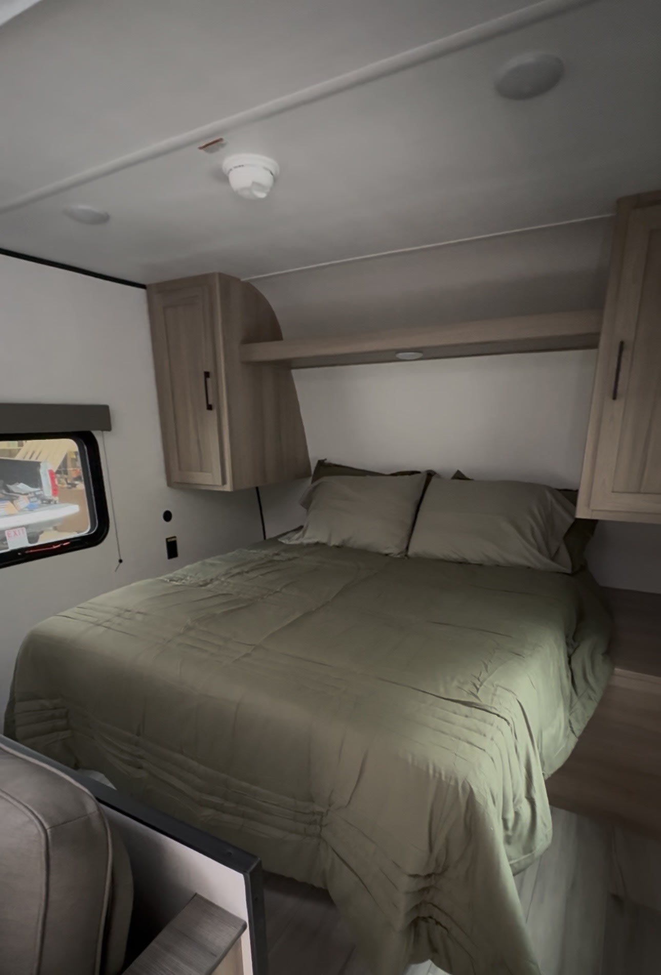 Comfortable RV rental bedroom with olive green bedding, overhead storage, and a window view, perfect for your next adventure.. Keystone RV Coleman 2025