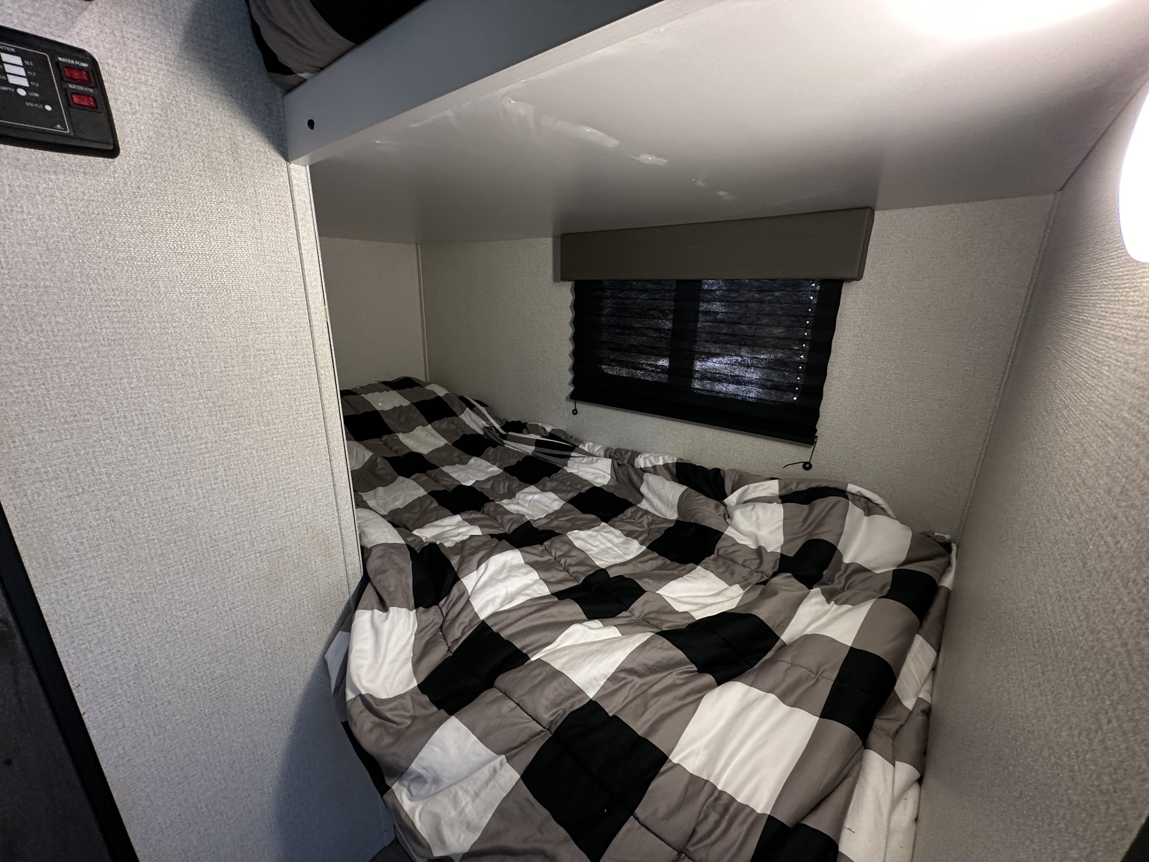 Inside an RV rental: a cozy bunk bed with a black, white, and gray plaid comforter, window blinds, and utility controls.. Keystone RV Hideout 2022