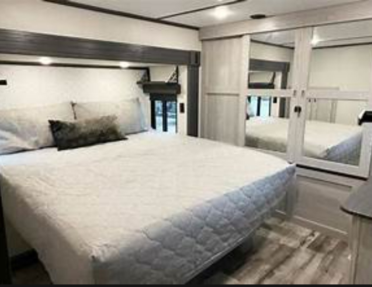 Modern RV rental bedroom, featuring a comfortable bed with a quilted comforter and mirrored closet doors for storage.. Keystone RV Montana High Country 2022
