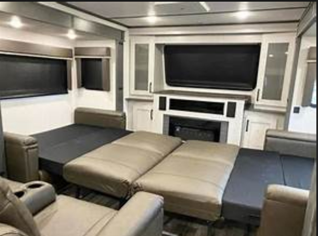 This rv rental living room features a partially extended sofa bed, an entertainment center with a fireplace, and windows, offering comfort.. Keystone RV Montana High Country 2022