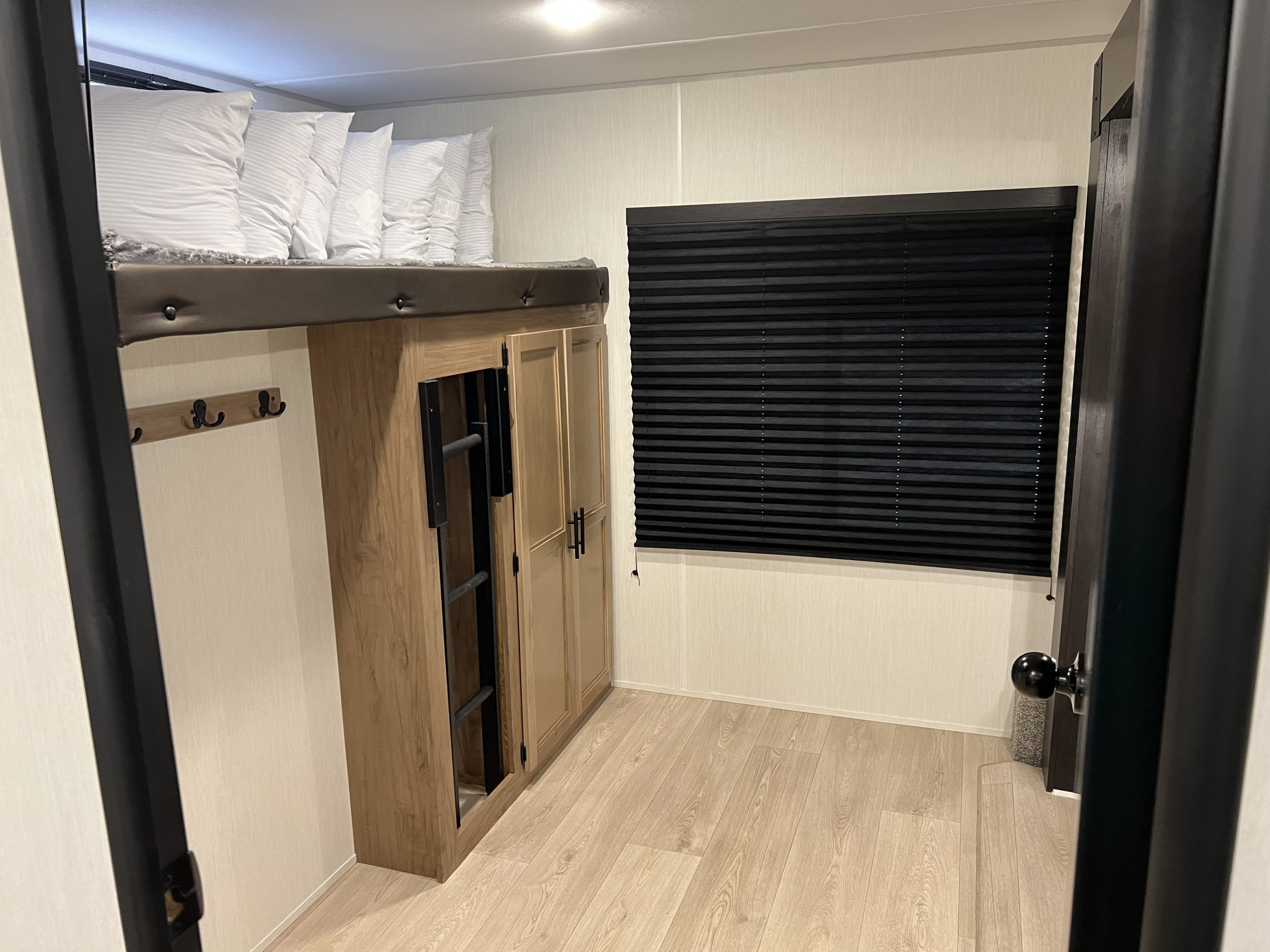 RV rental: Cozy bunk bed with pillows, integrated ladder & storage cabinet, plus a window with black blinds. Functional space.. Forest River Cherokee Wolf Den 2025