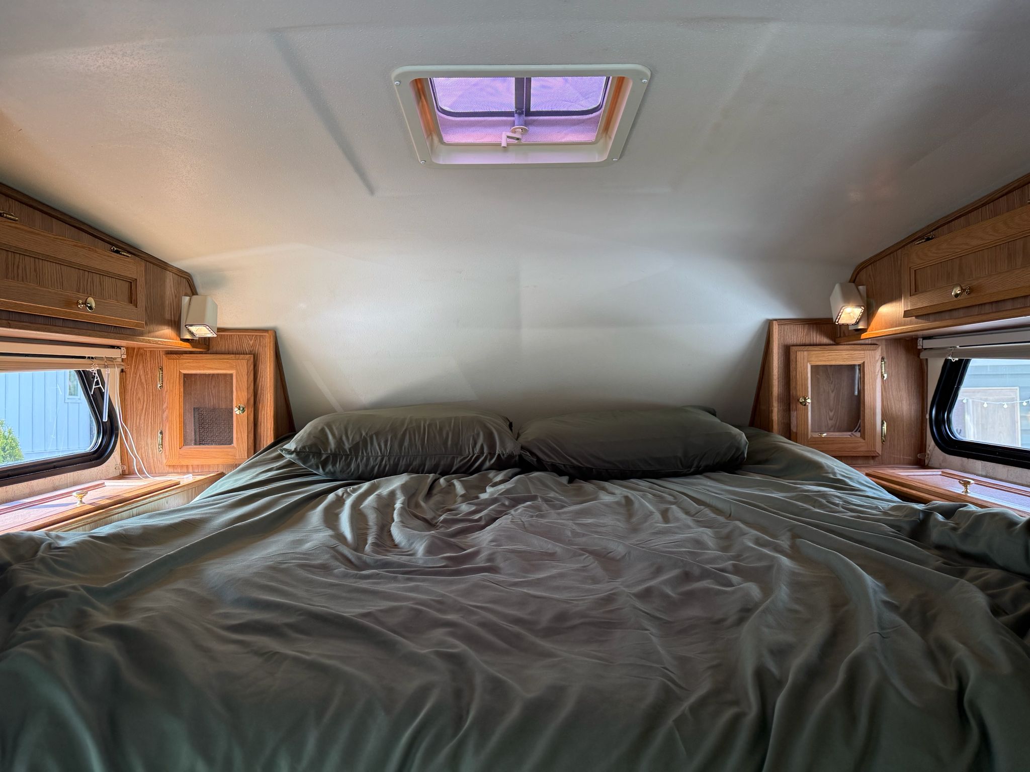 Inside this inviting RV rental bedroom: a bed with green sheets, wood cabinets, windows, and an overhead vent.. Chevrolet Silverado 3500 Classic 2007