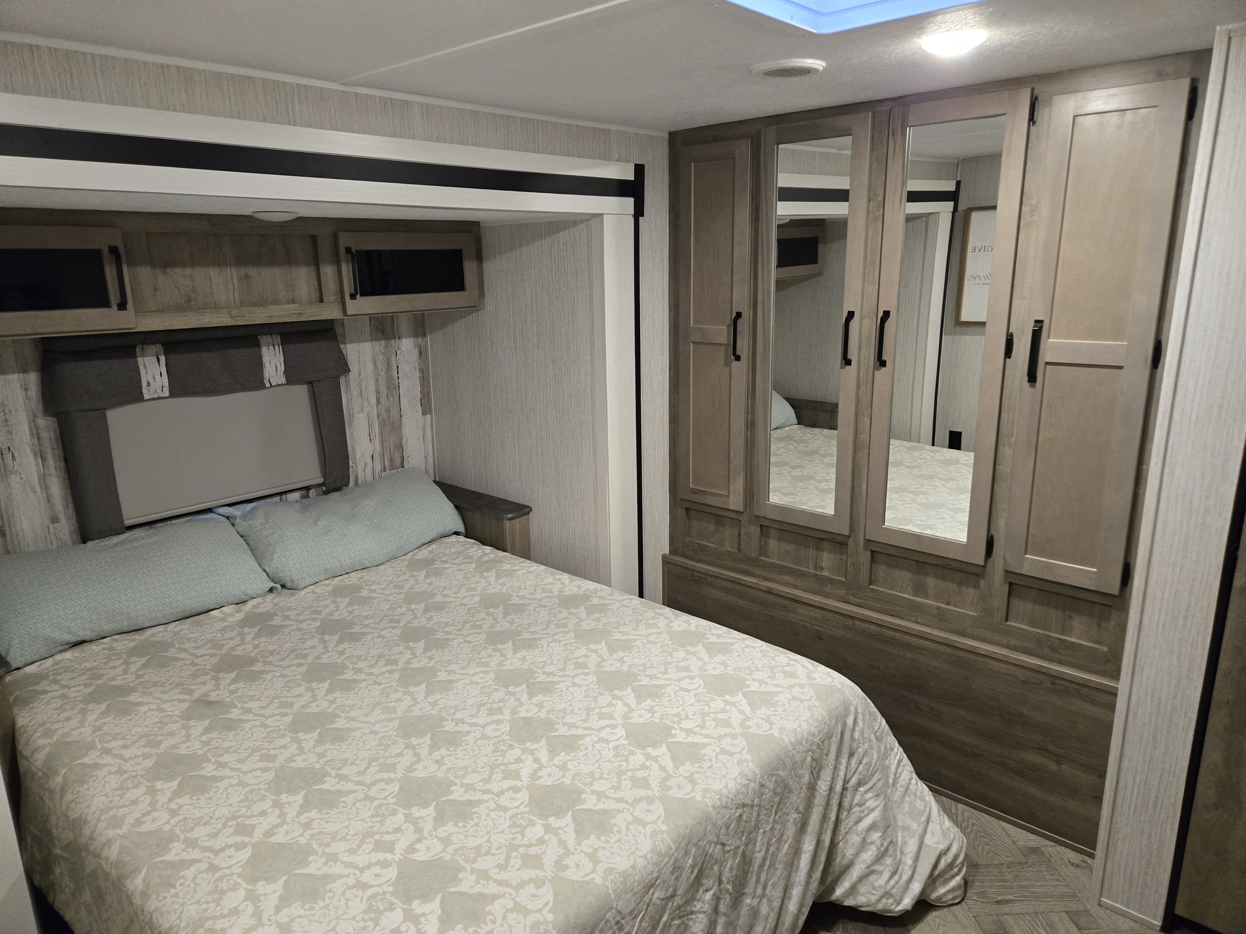 Modern RV rental bedroom features a comfy bed, overhead storage, and a stylish wardrobe with mirrors.. Forest River Palomino Puma 2022