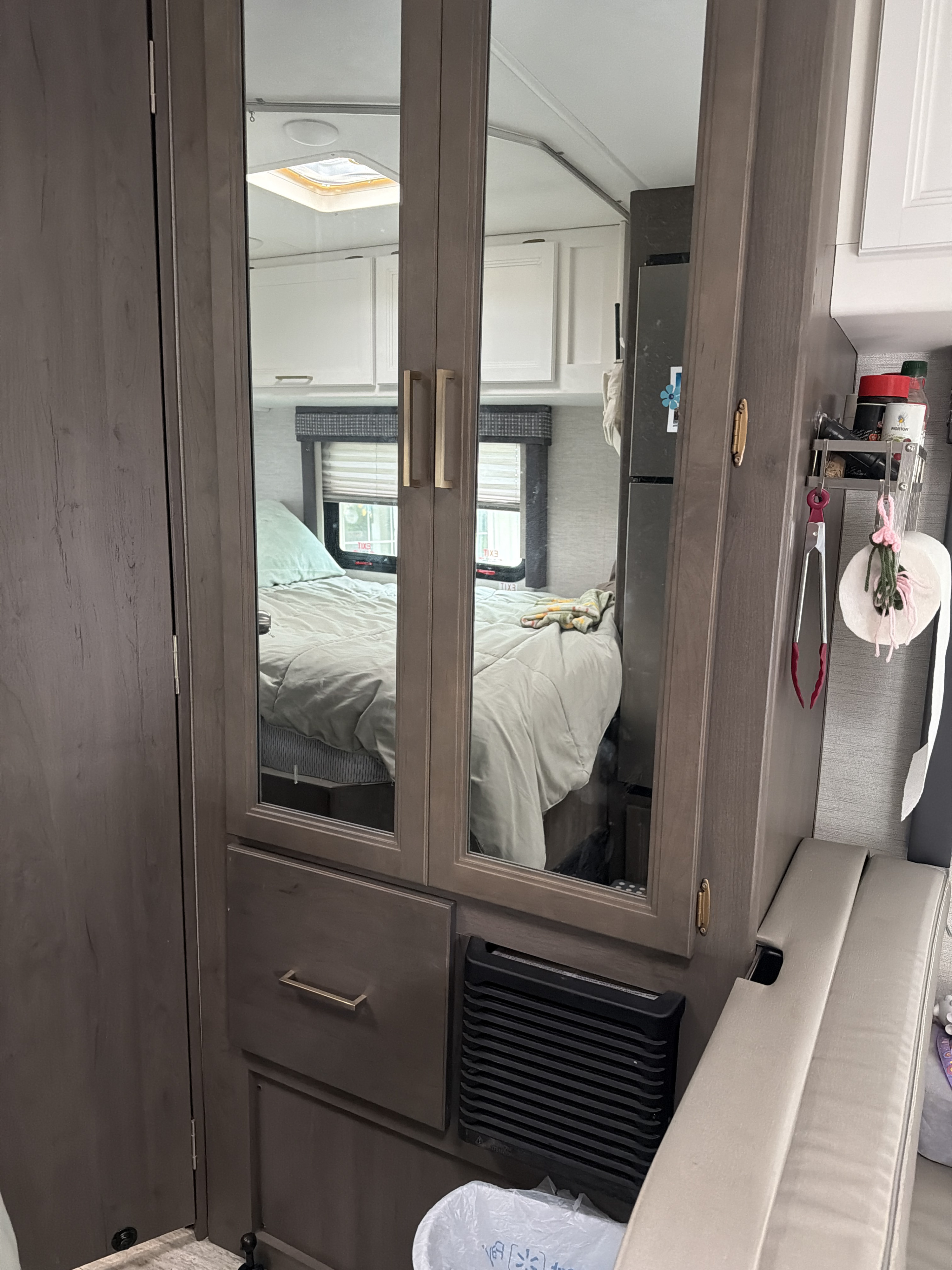 Inside an RV rental, showing a mirrored closet reflecting the bedroom with a bed and window, alongside a compact kitchen area.. Thor Chateau 2024