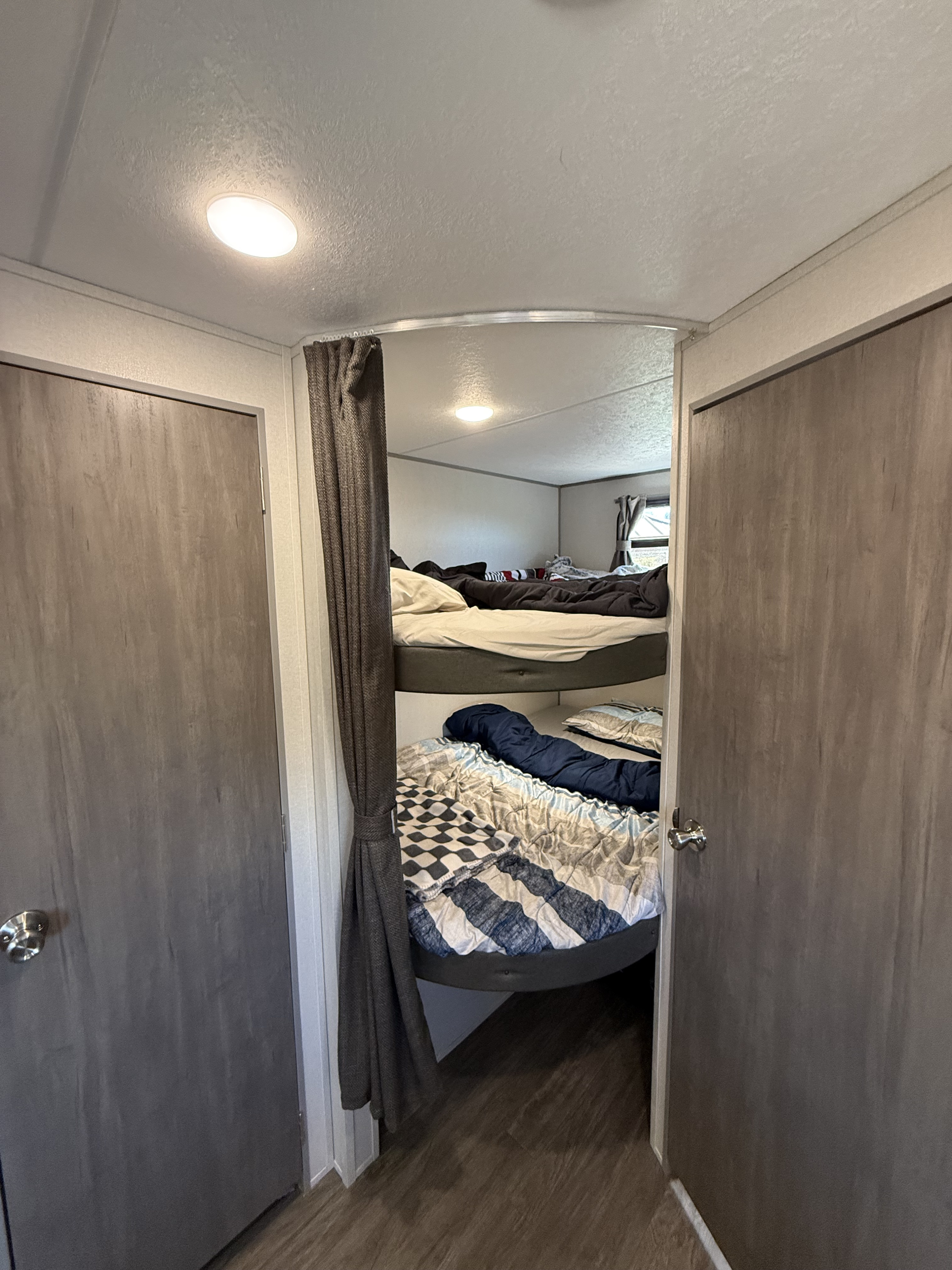 Inside an RV rental, two stacked bunk beds are visible, complete with bedding, offering a compact sleeping area with a privacy curtain.. Forest River Aurora Aurora Light 2025