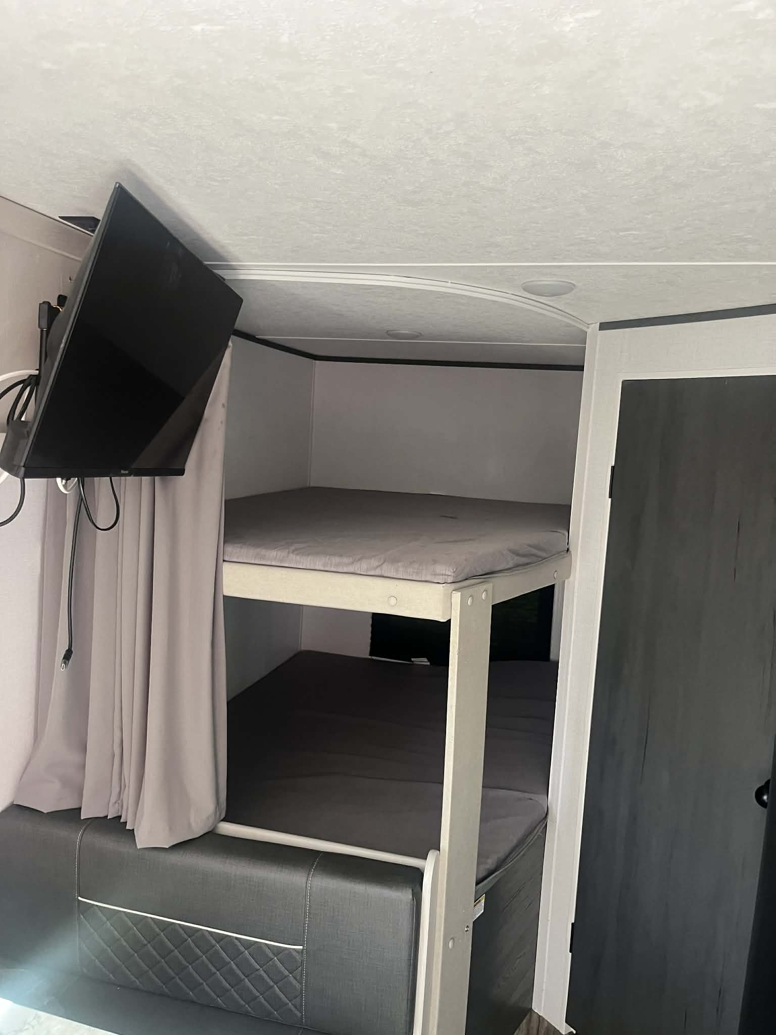 Inside an RV rental, this compact area features cozy gray bunk beds, a wall-mounted TV, and a quilted seating bench.. Dutchmen Aspen Trail 2023
