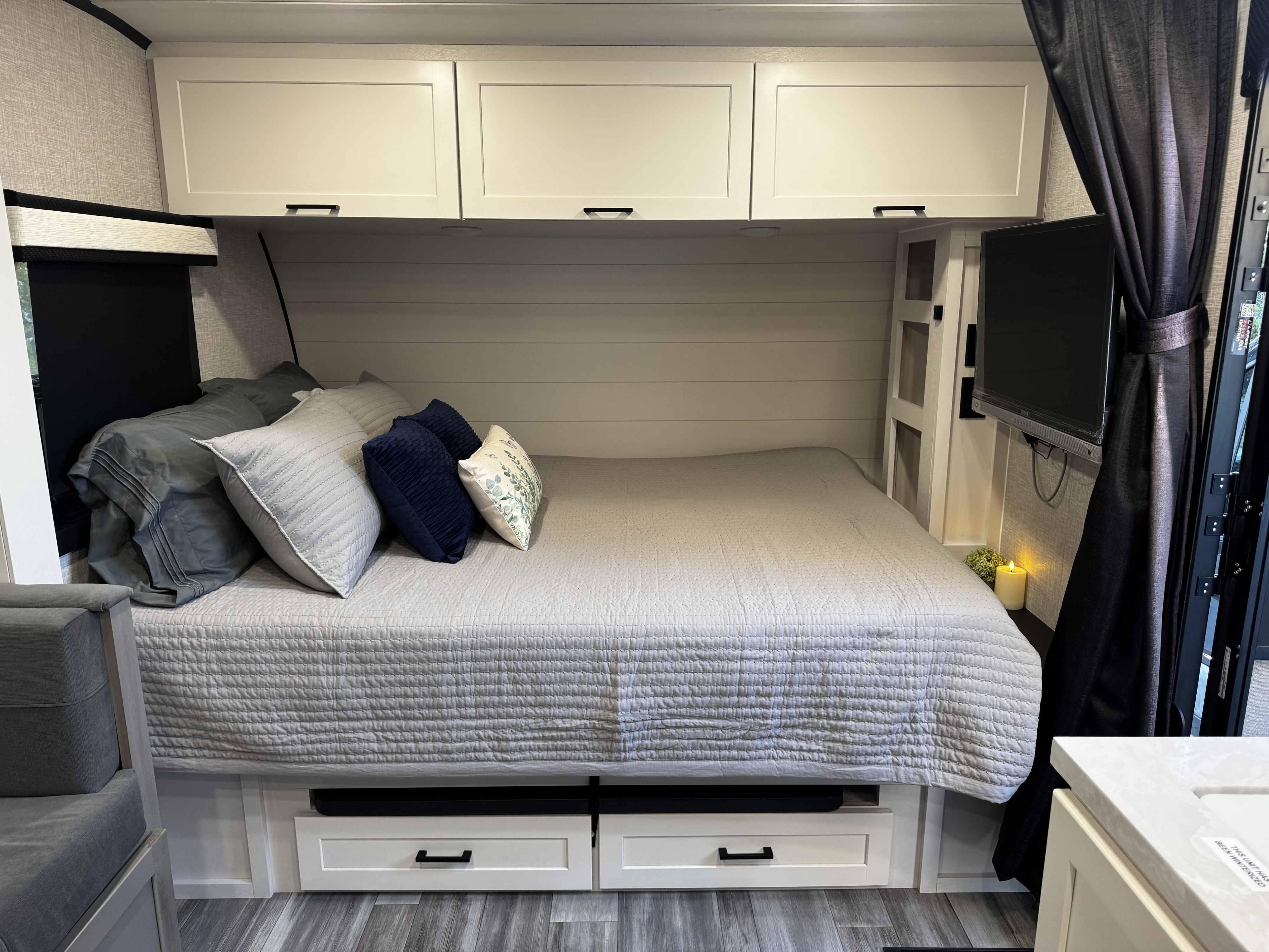 This comfortable, modern RV rental bedroom features a cozy bed, overhead cabinets, under-bed storage, and a wall-mounted TV.. Jayco Jay Feather Micro 2025