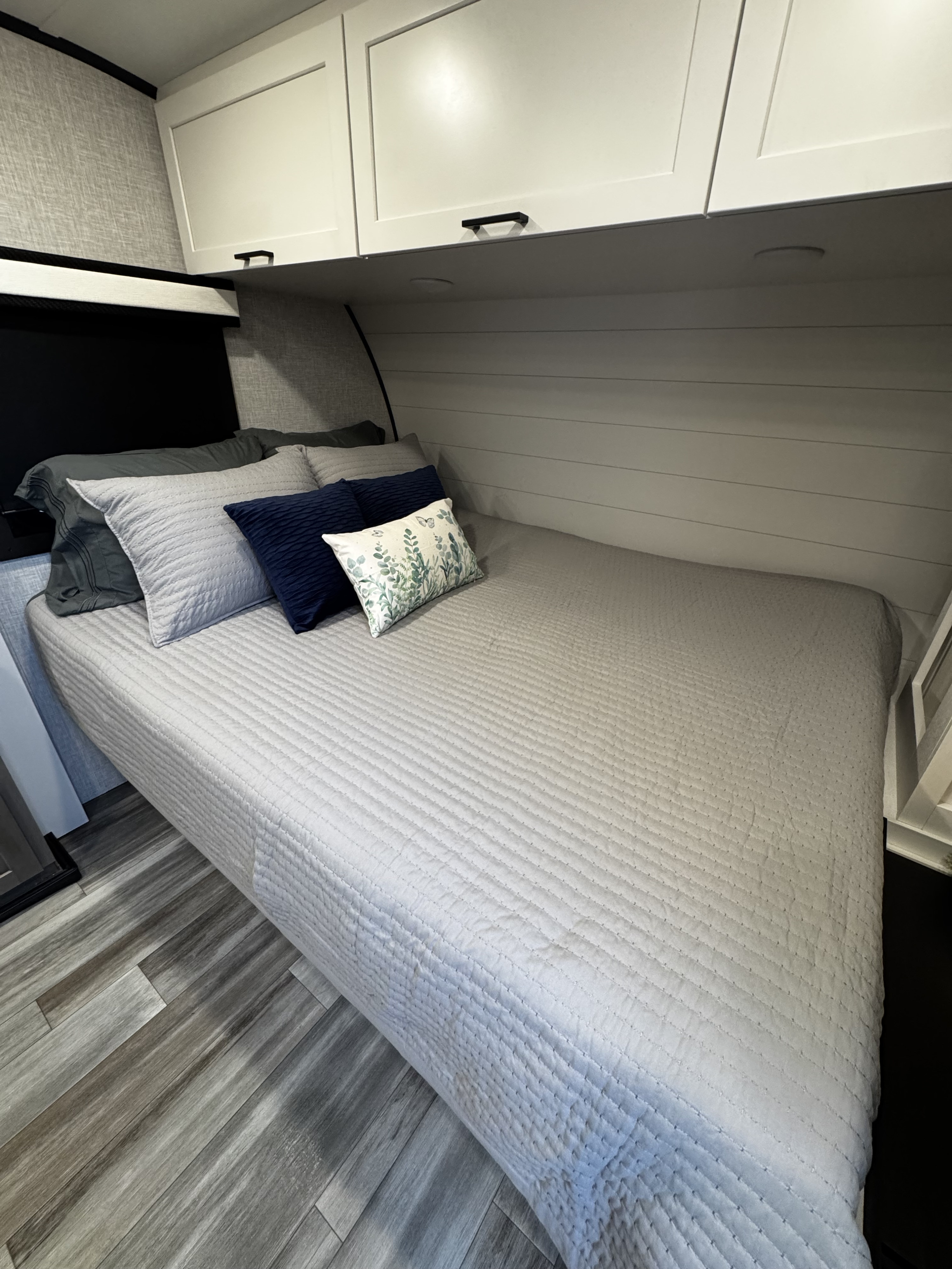 RV rental interior: A cozy bedroom with a grey quilted bed, assorted pillows, white overhead cabinets, and modern wood-look flooring.. Jayco Jay Feather Micro 2025