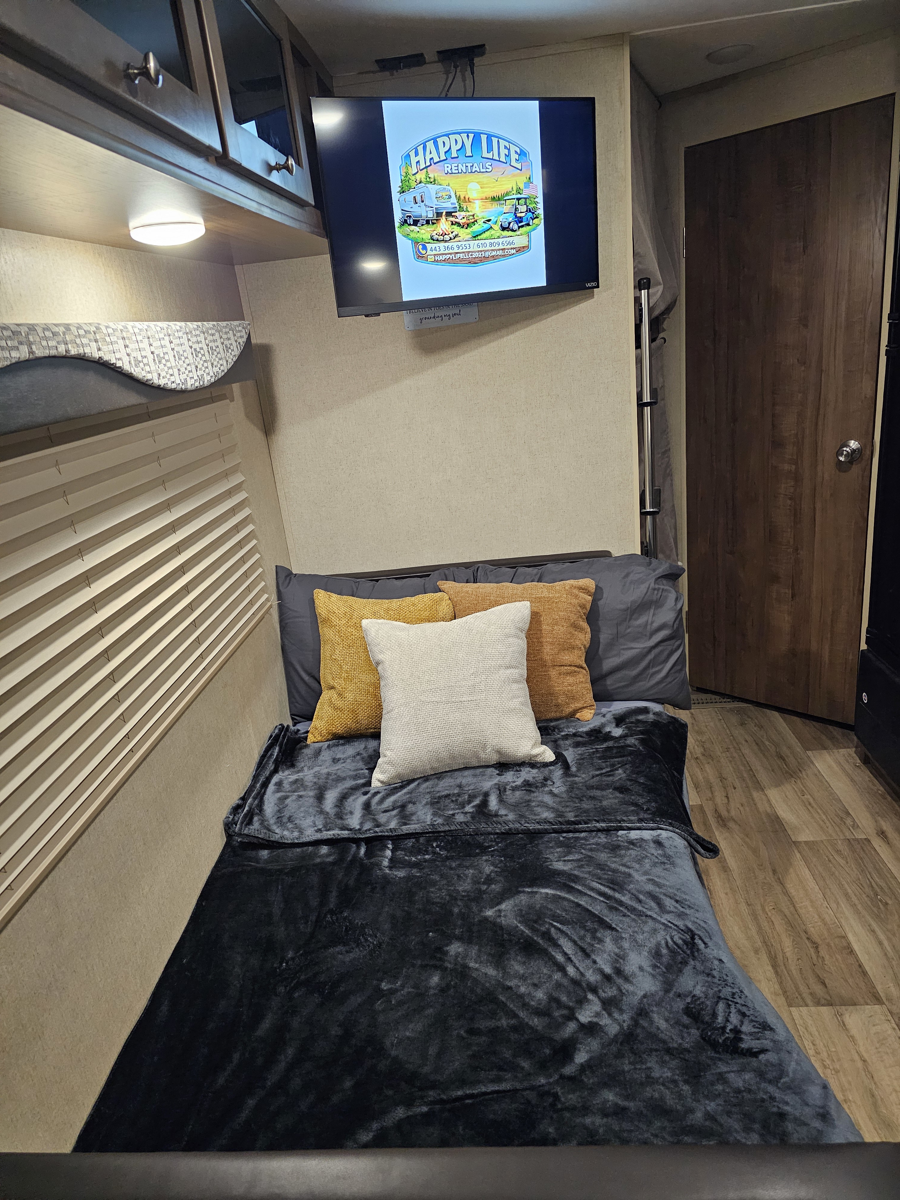 This cozy RV rental features a bedroom with a comfortable bed, overhead bunk, and a TV displaying the Happy Life Rentals logo.. Aspen Trail Aspen Trail Trailer 2018