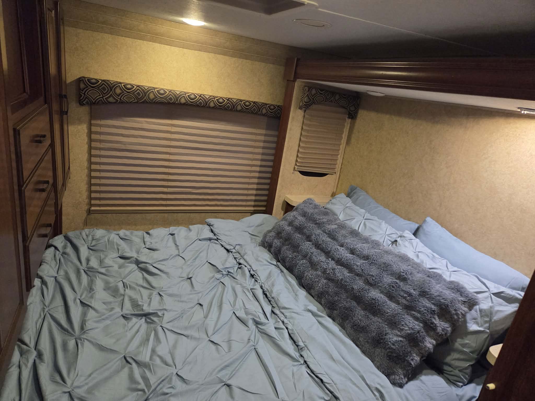 Relaxing RV rental interior: bedroom with comfy light blue bedding, fluffy grey pillow, window blinds, and wood cabinetry.. Forest River Sunseeker 2014