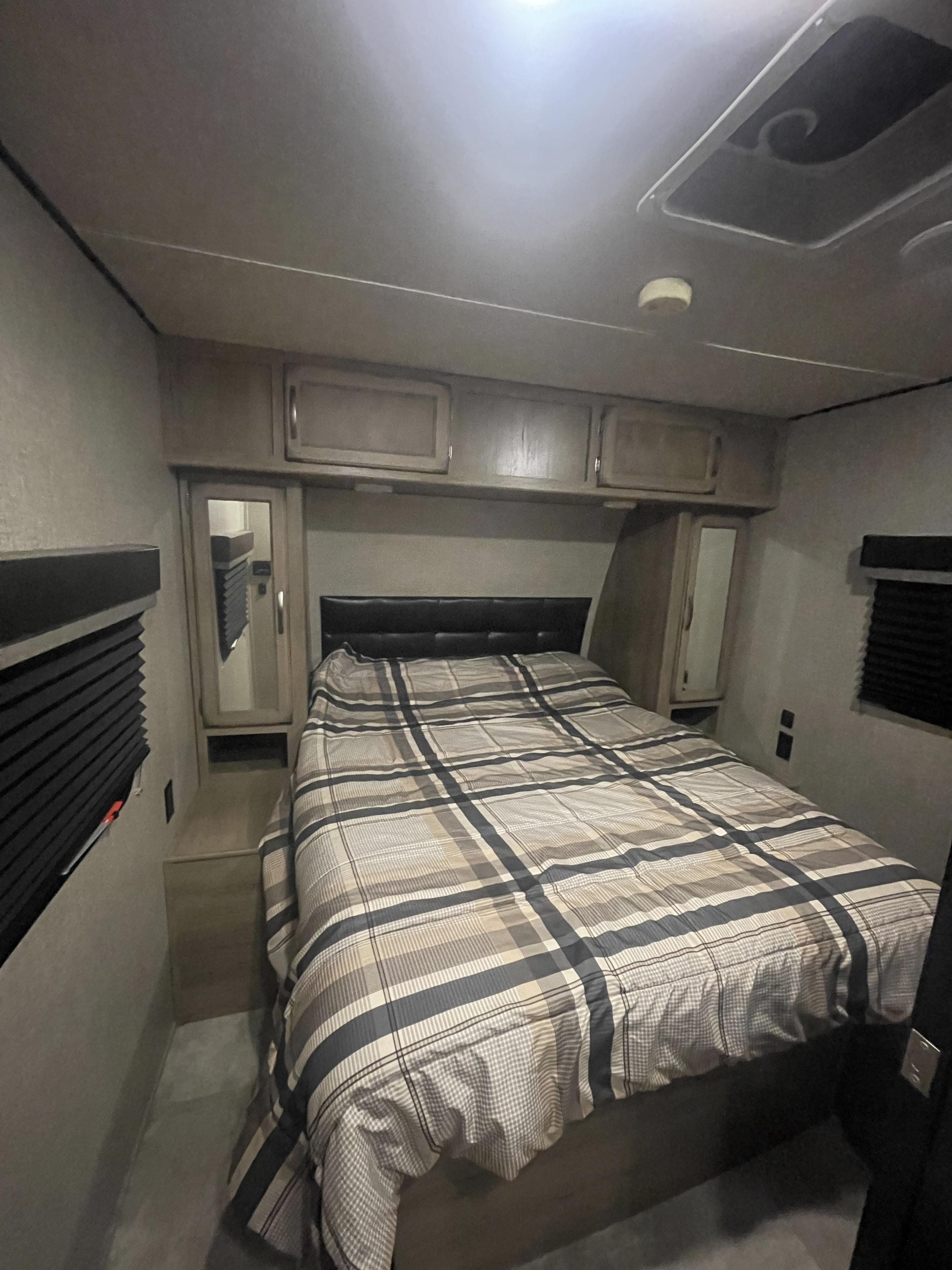 Cozy RV rental bedroom with a plaid bed, overhead cabinets, mirrored wardrobes, and window blinds for privacy on your journey.. Grand Design Transcend 2019