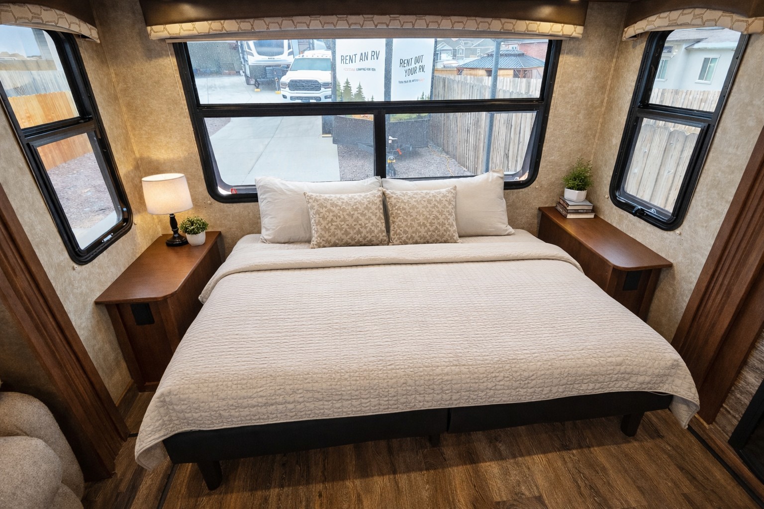 Inside an RV rental, a comfy bedroom features a queen bed, nightstands with decor, and large windows revealing an outdoor scene.. Highland Ridge RV Open Range Roamer 2017