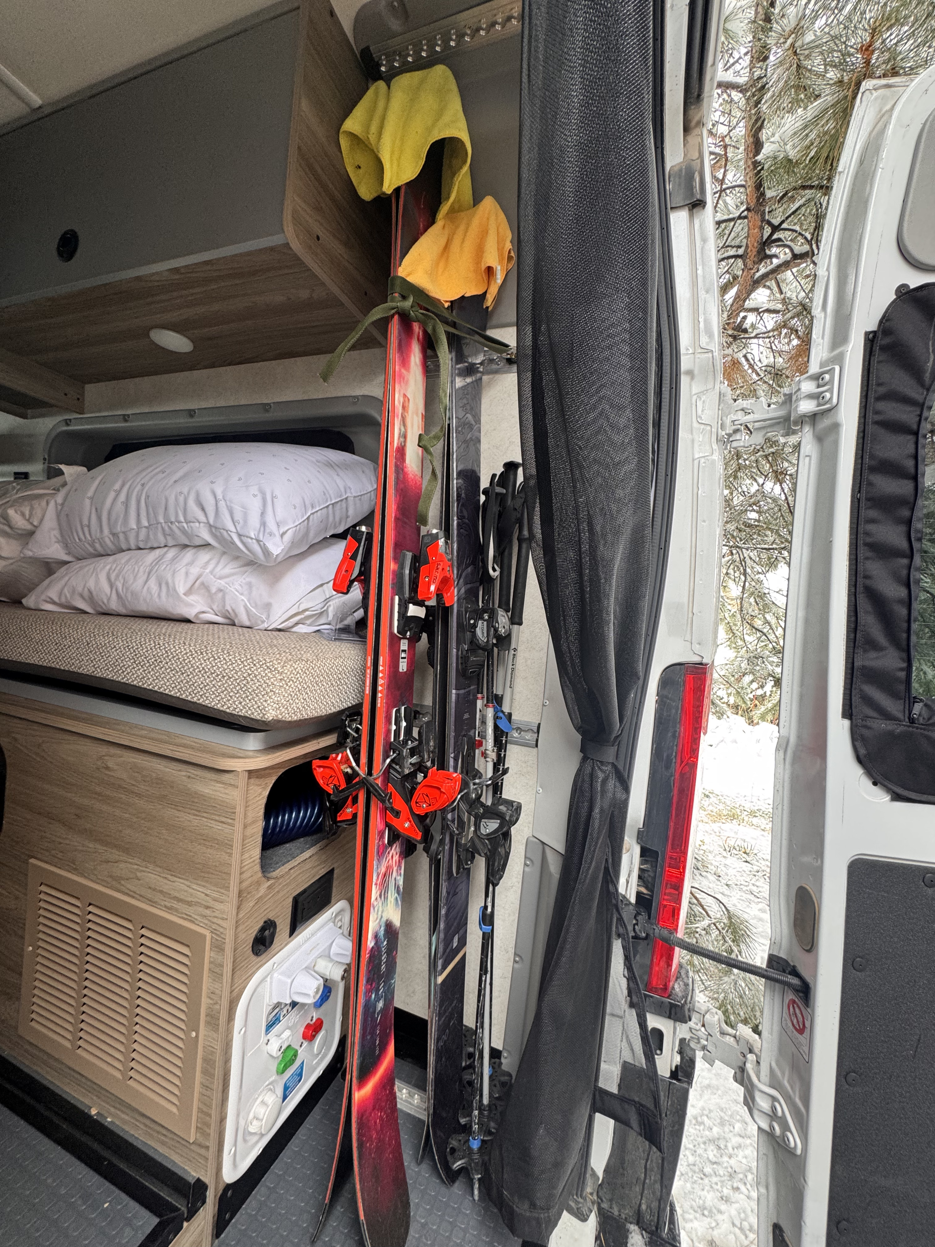 RV rental interior: Skis, poles, & bedding neatly stored in a camper van for a winter adventure, with snowy trees visible outside.. Winnebago Solis 2025