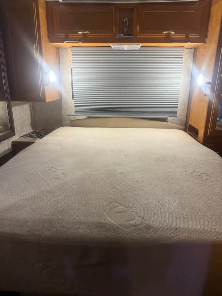 RV rental bedroom featuring a comfy bed, overhead cabinets, and window blind, perfect for your next adventure.. Gulf Stream Gulfstream 1999