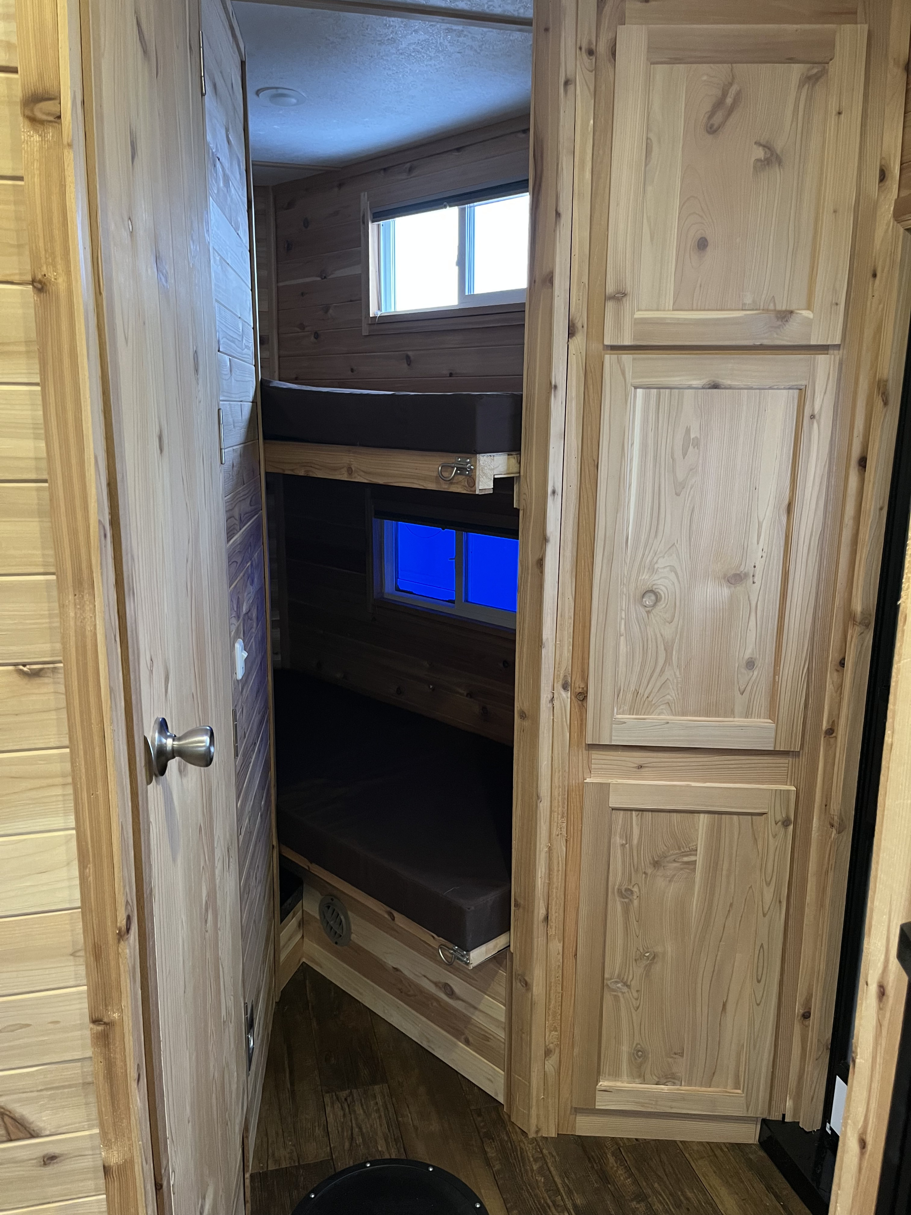 RV rental's rustic interior: wooden bunk beds, bright windows, and ample cabinets. A cozy, compact camper space.. Ice Castle Fish Houses Ice Castle Fish Houses Trailer 2023