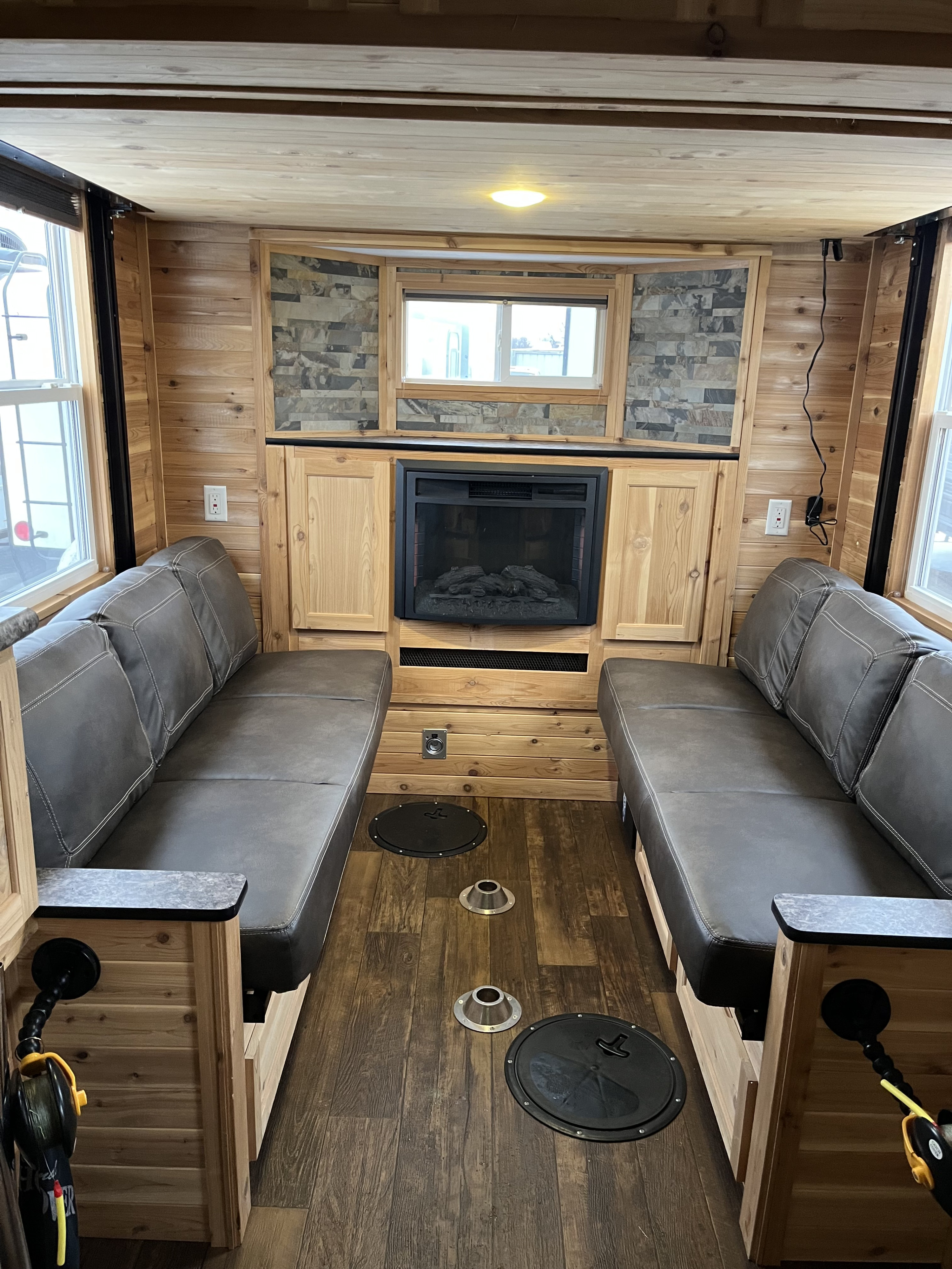 Cozy RV rental interior: wood-paneled ice fishing house with benches, fireplace, and fishing holes on the floor.. Ice Castle Fish Houses Ice Castle Fish Houses Trailer 2023