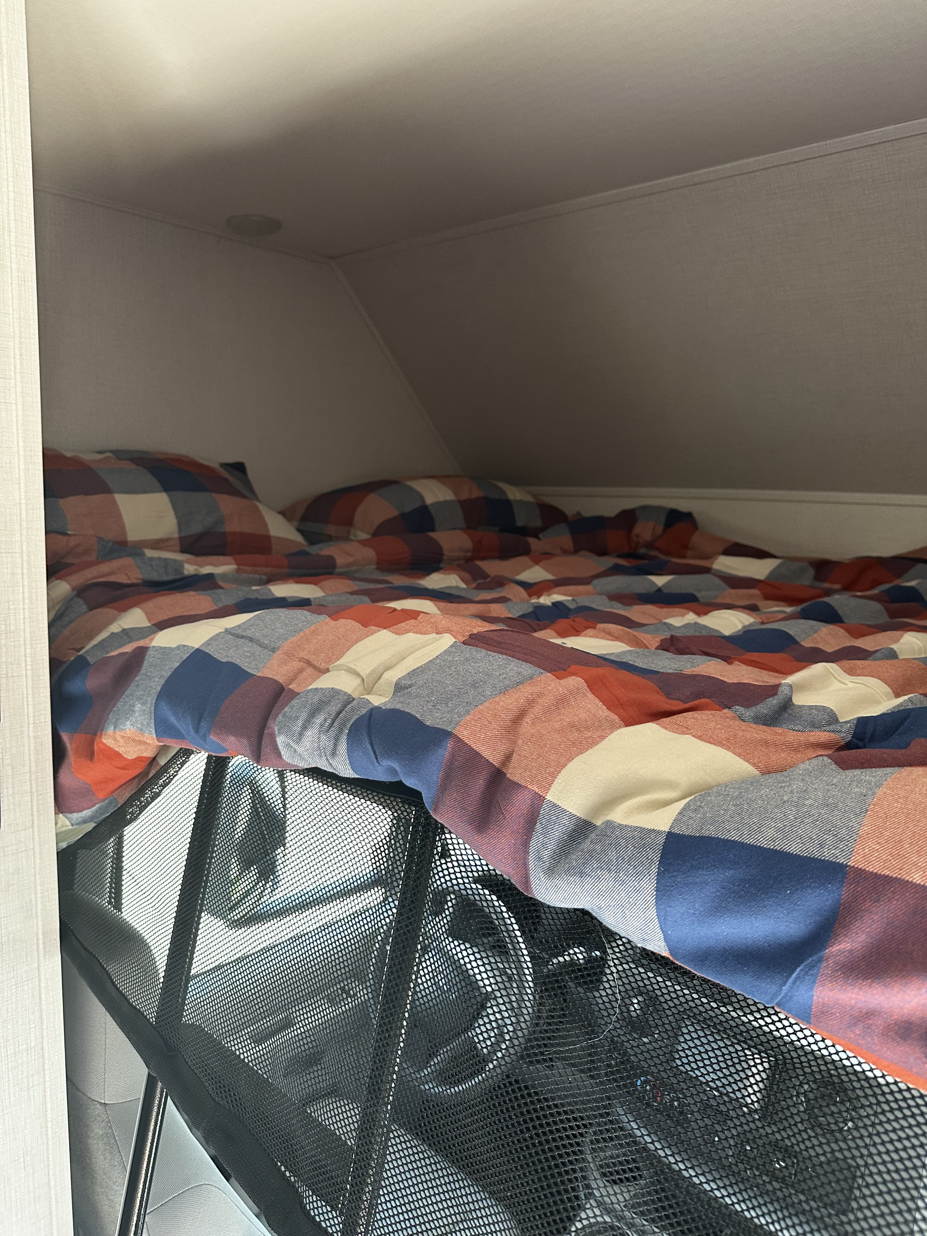 Cozy RV rental cab-over bed with plaid bedding and safety net above the driver's area, inviting a restful journey.. Forester LE 2026