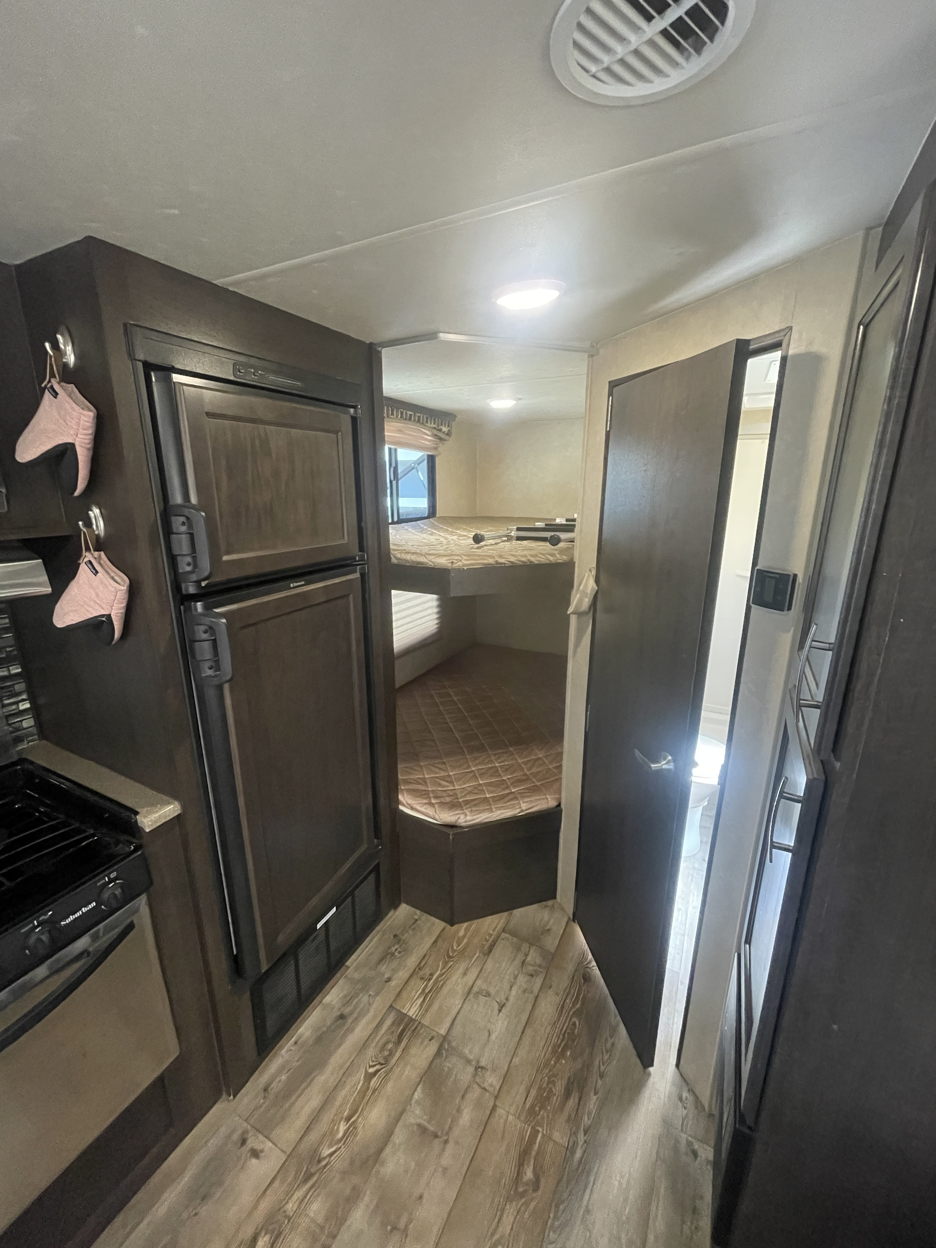 Cozy RV rental interior showing kitchen with fridge/stove, bunk beds, and bathroom entry. Wood-look flooring.. Forest River Sonoma 240 BHS 2017