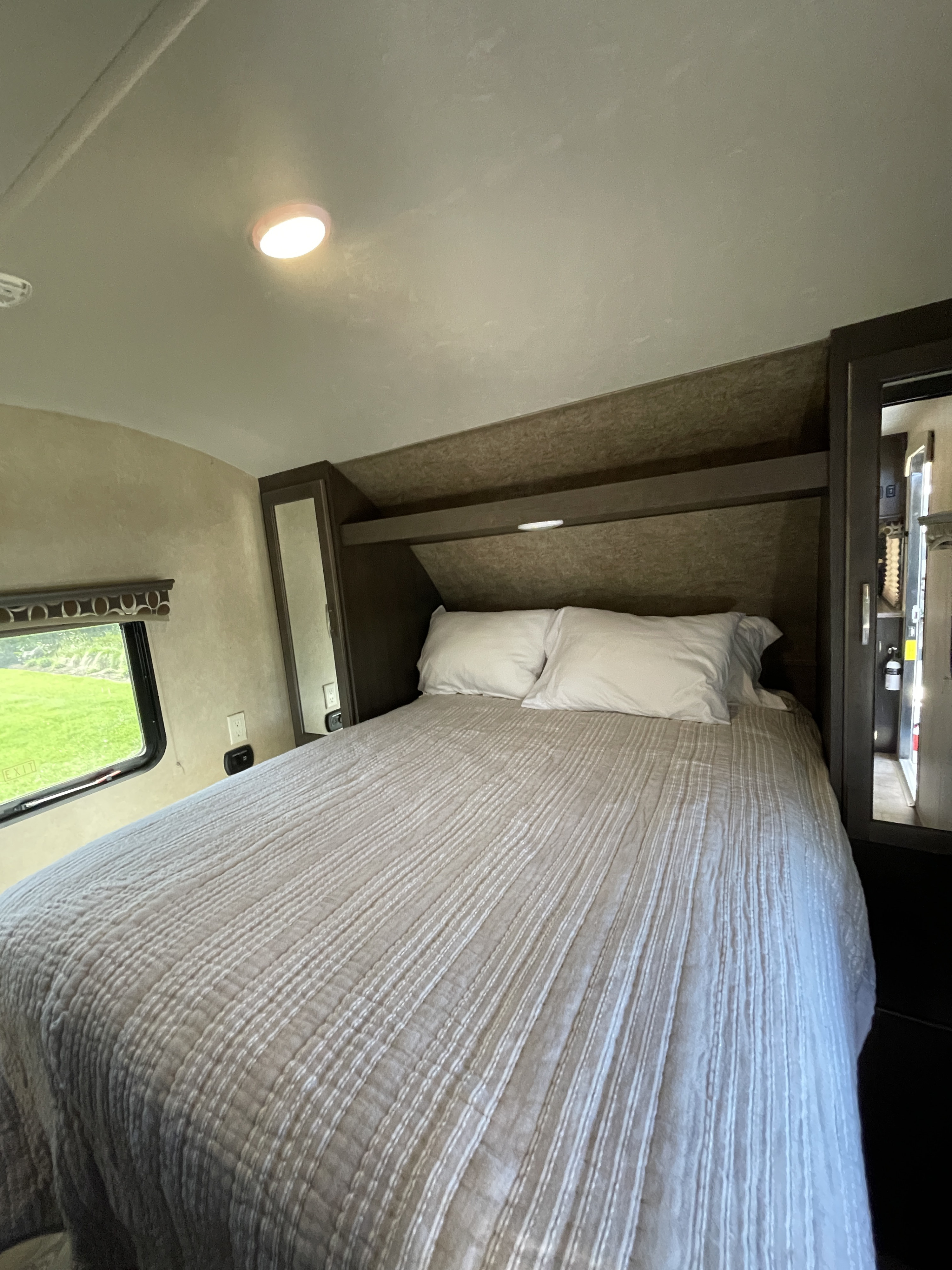 RV rental bedroom with a striped comforter, white pillows, window with a green view, and dark wood cabinetry.. Forest River Sonoma 240 BHS 2017