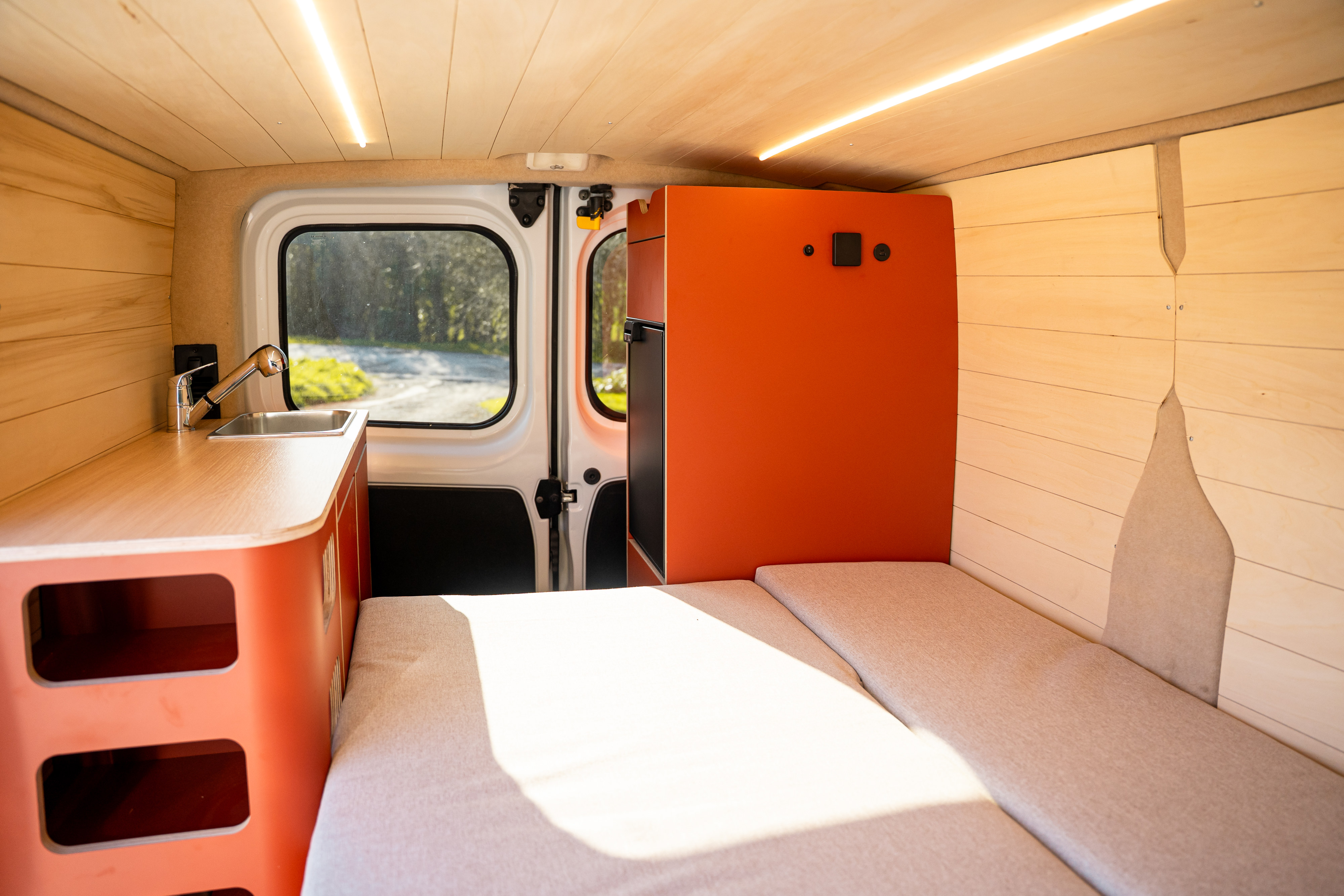 Modern rv rental interior with a light wood ceiling, kitchen sink, and comfortable bed area.. Renault Trafic 2019