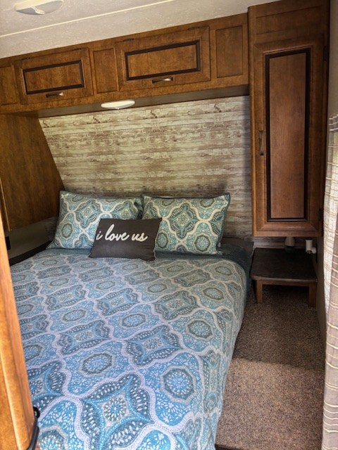 Comfortable RV rental bedroom interior with blue patterned bedding, wooden cabinets, and a rustic headboard.. Crossroads RV Zinger 2017