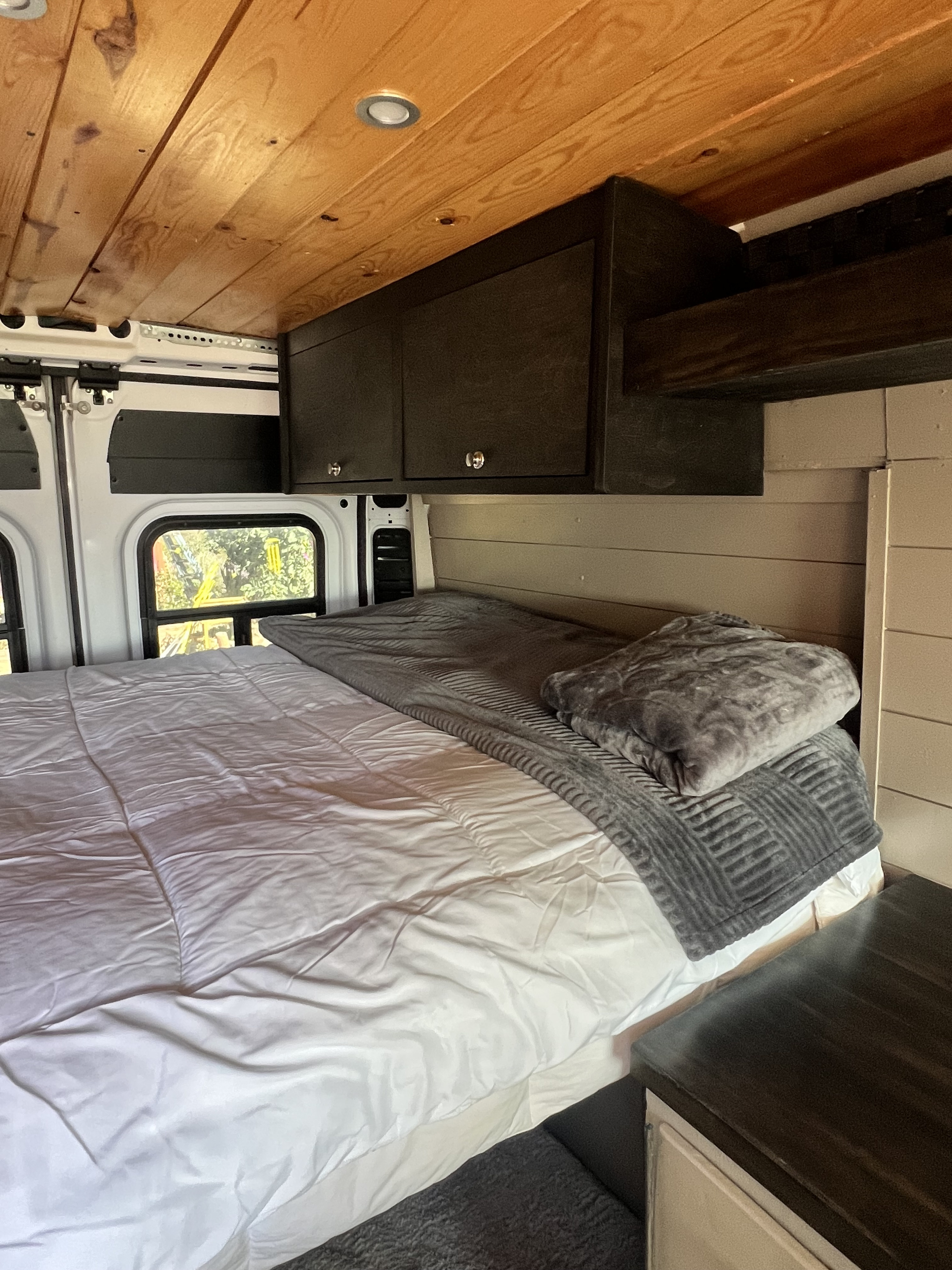 This RV rental features a cozy bedroom with a wooden ceiling, comfy bed, storage, and natural light from a window.. Dodge ProMaster 2500 2020