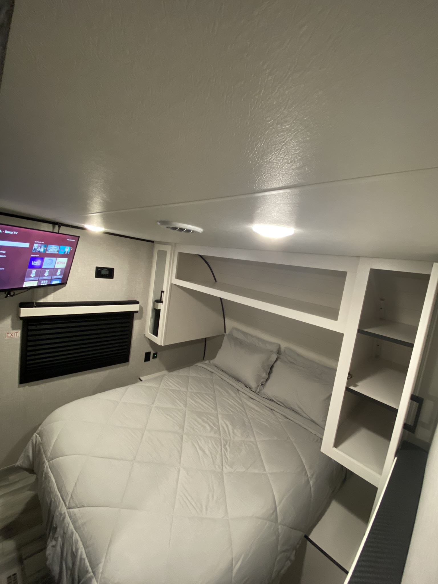 Modern RV rental bedroom featuring a cozy queen bed, mounted TV, and ample overhead storage. Enjoy a comfortable stay!. Jayco Jay Flight SLX 2025