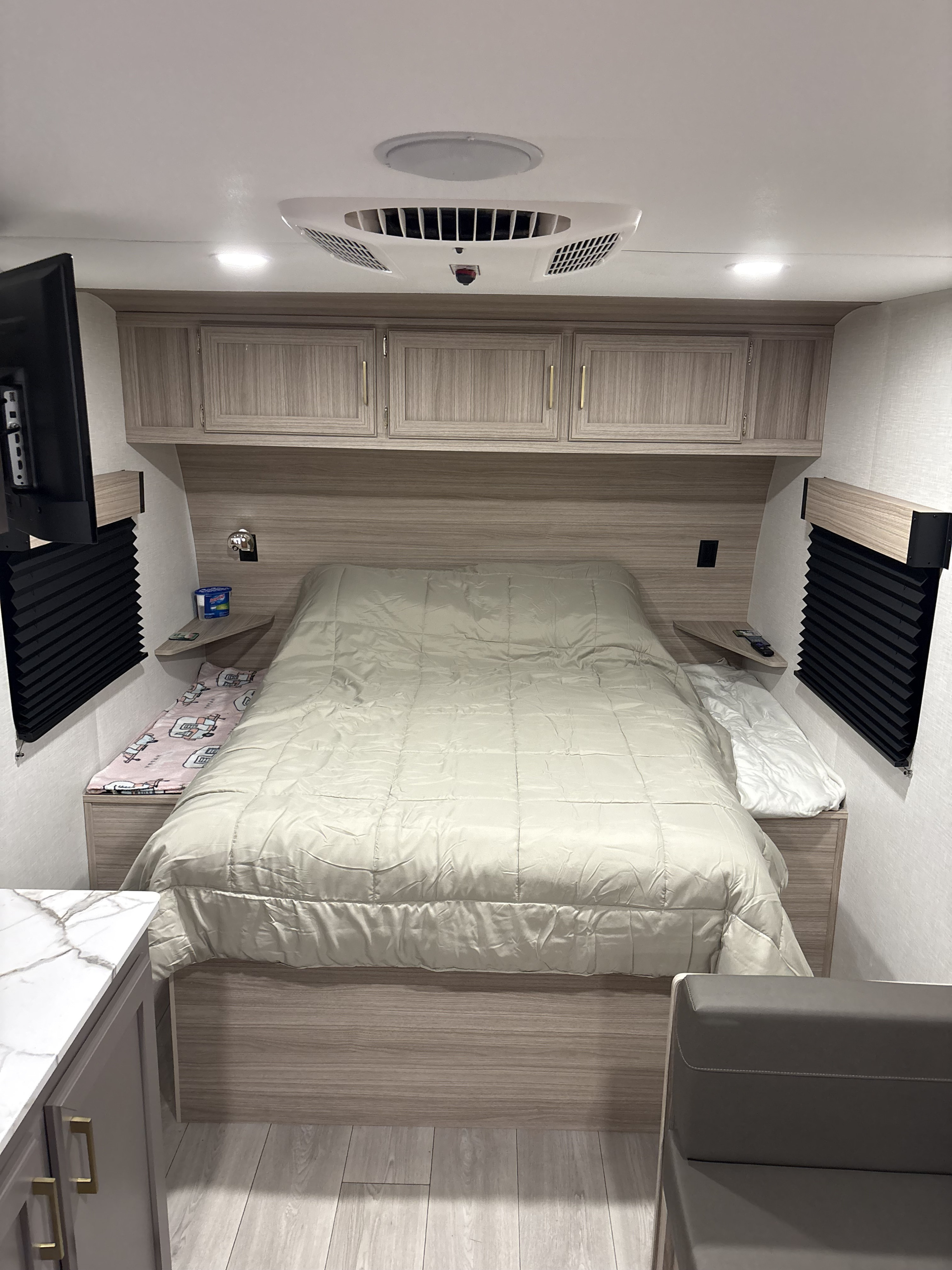 Cozy RV rental bedroom featuring a bed with light comforter, overhead cabinets, wall-mounted TV, and air conditioning. Ideal for travel comfort.. KZ Sportsmen Classic 2026