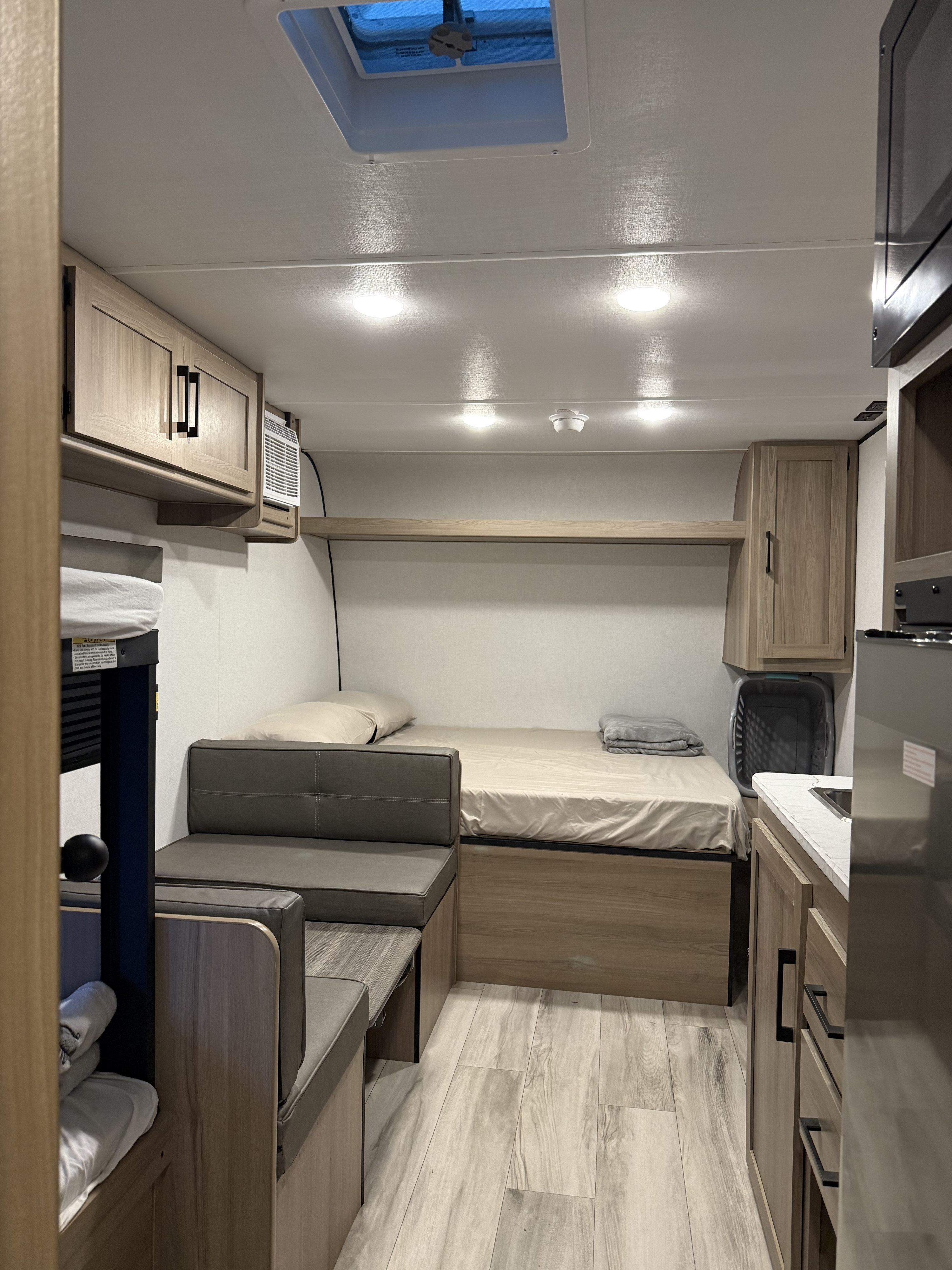 Inside your next RV rental: a modern, compact living space with a bed, dinette seating, small kitchen, and storage.. Keystone Coleman 17B 2026