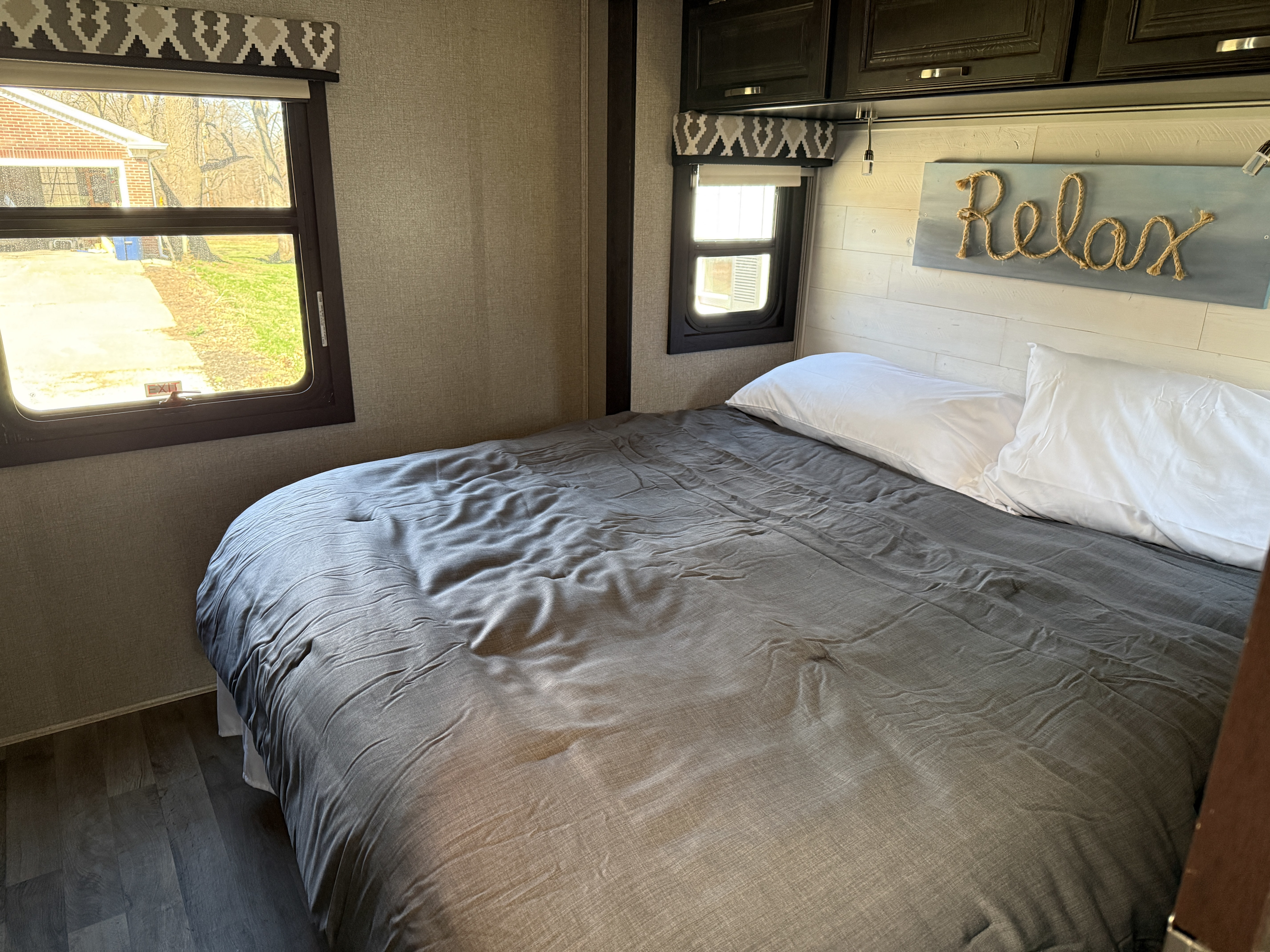 Cozy RV rental bedroom features a comfortable bed, views from windows, and a "Relax" sign. Perfect for your next adventure.. Jayco Precept 2021