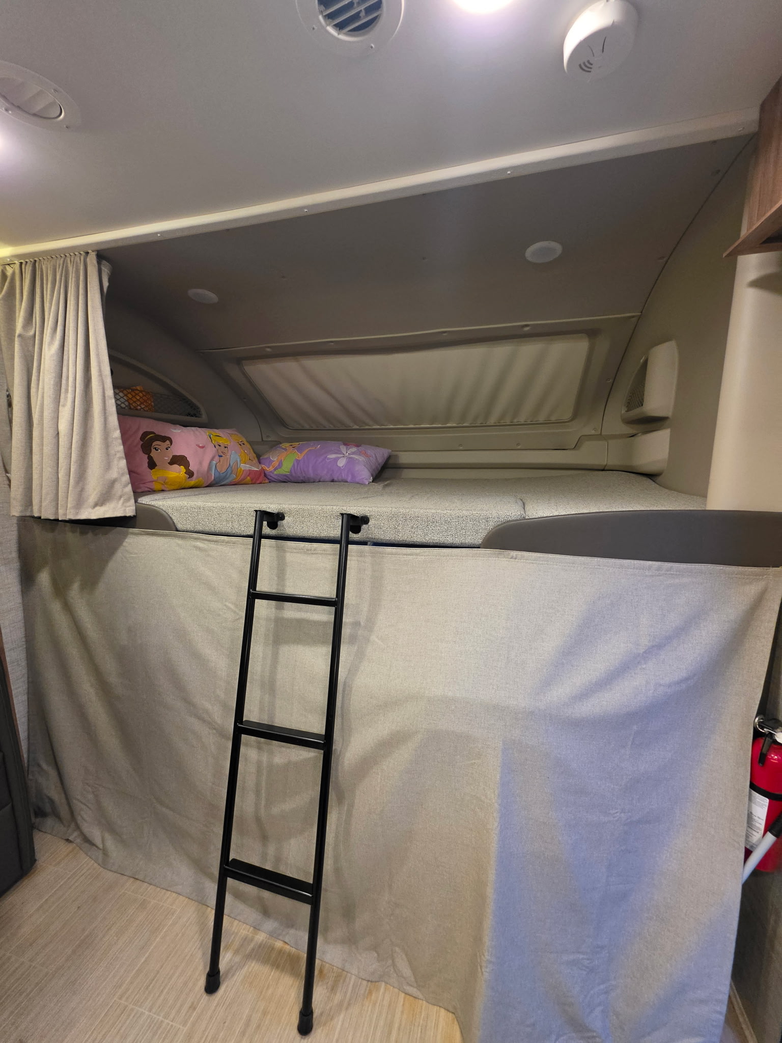 Over-cab bunk in an RV rental, showing a bed with pillows, ladder, privacy curtains, and ceiling features.. Entegra Coach Odyssey 2022