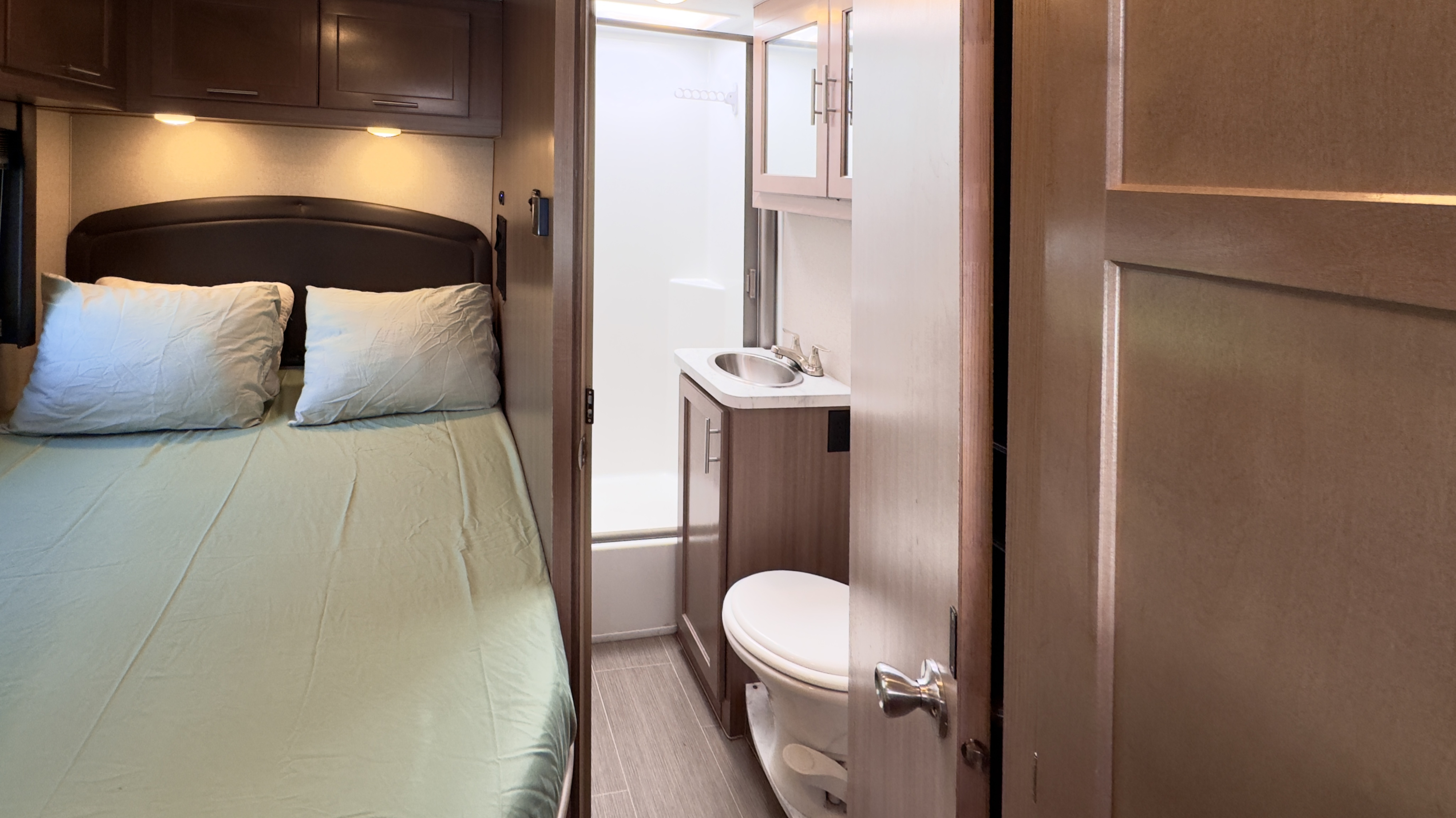 Cozy rv rental interior featuring a comfortable bed on the left and a compact bathroom with sink, toilet, and shower on the right.. Ford Adventurer 2021