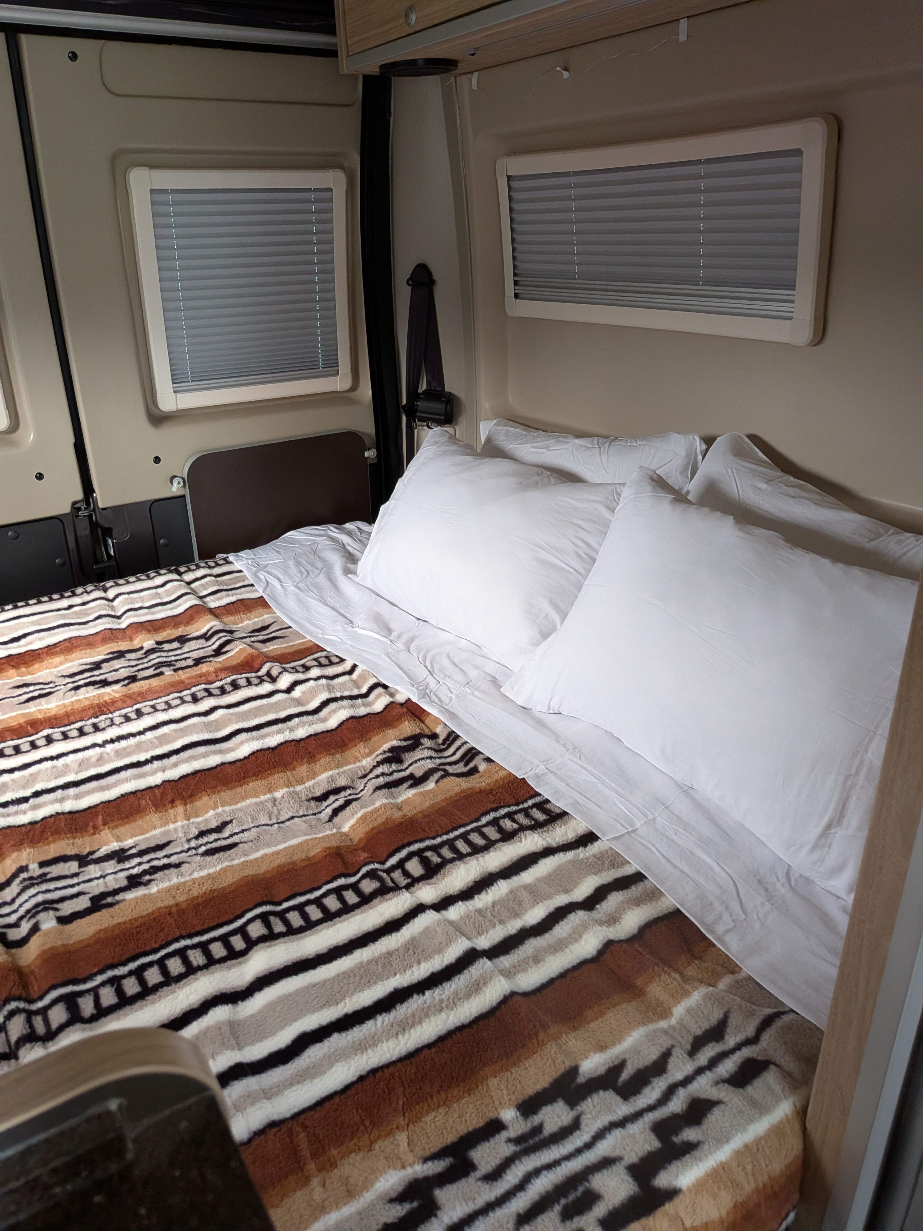 Cozy rv rental bedroom showing a bed with a striped blanket and white pillows, with window blinds and vehicle interior details.. Hymer Hymer Class B 2018