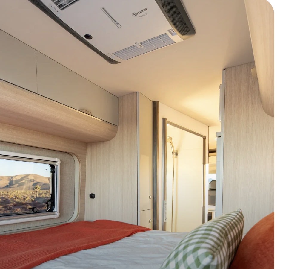 RV rental's cozy bedroom features a bed, desert window view, overhead AC, and a compact shower stall. Perfect for travel.. Noovo Noovo Class B 2024