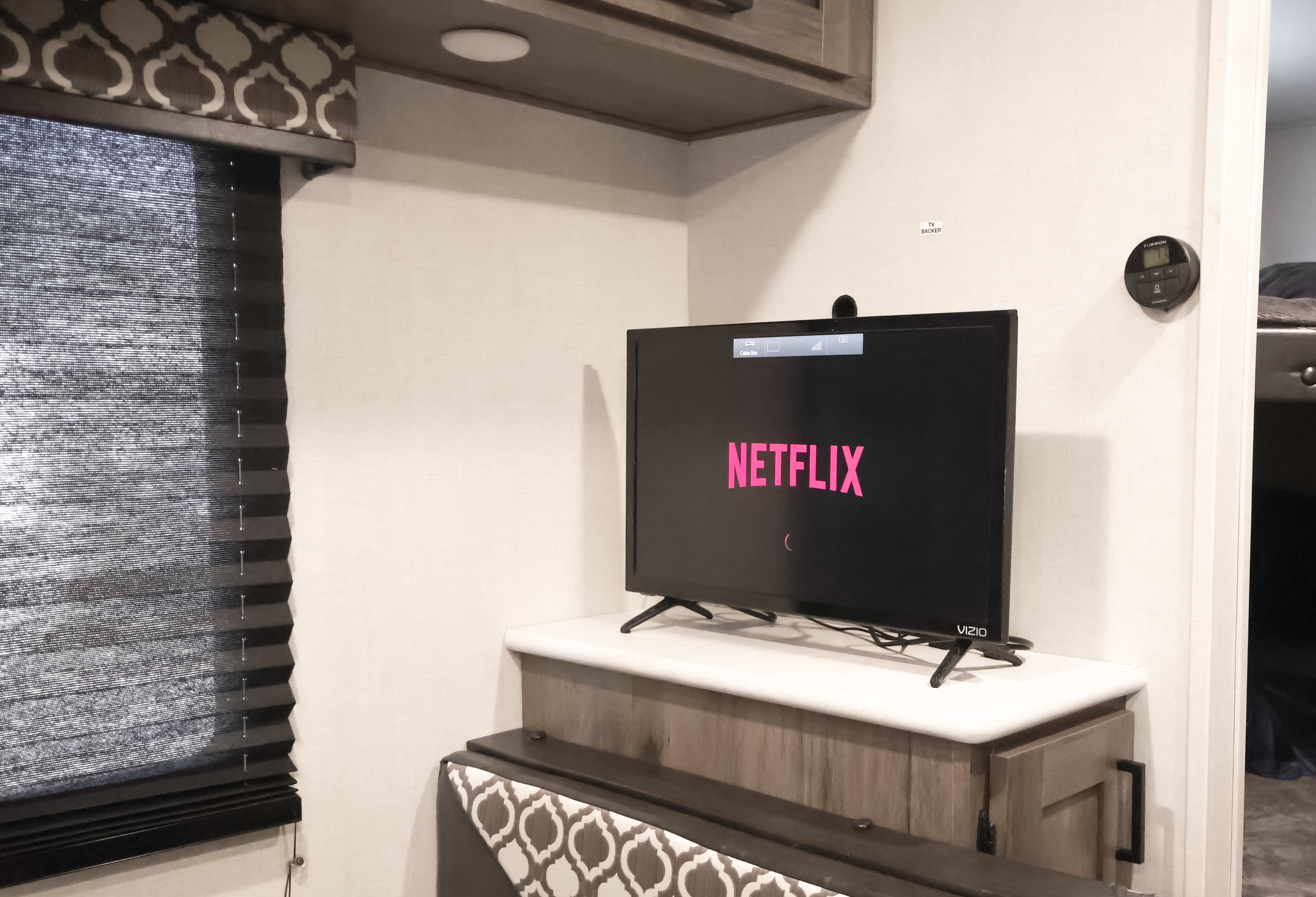 An RV rental living space with a Vizio TV showing Netflix, surrounded by modern cabinetry, blinds, and a climate control unit.. Forest River Tracer LE 2021