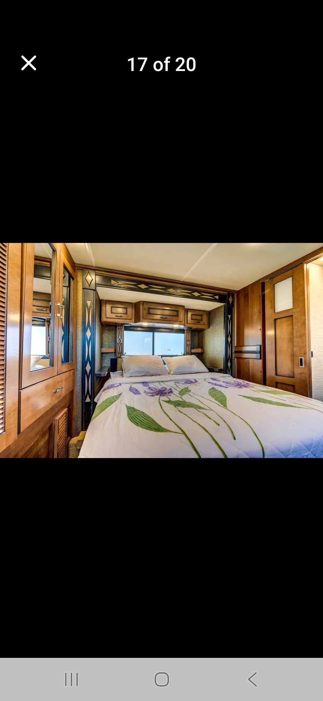 RV rental bedroom featuring a cozy bed with floral duvet, wood cabinetry, and a window view.. Fleetwood Excretion 2015