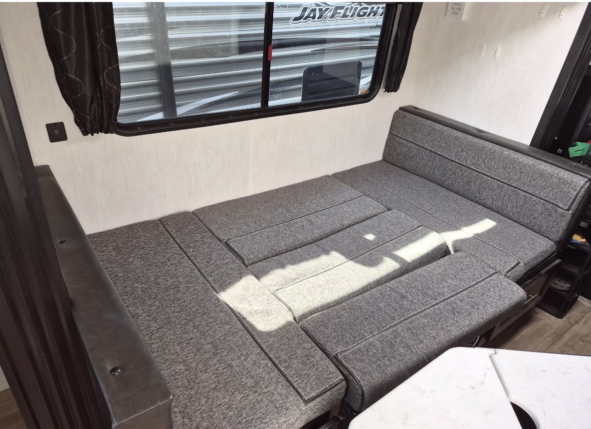 Inside an **rv rental**: a comfortable gray dinette converts into a bed, offering a cozy sleeping space with a window and charging port.. Forest River Cherokee 2022