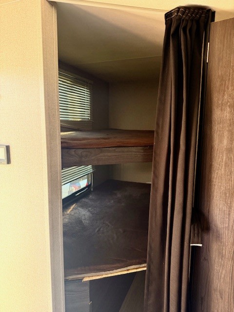Cozy RV rental bunk beds with windows and a privacy curtain, providing a comfortable sleeping area in this vehicle's interior.. Kodiak Ultimate 288BHSL 2018